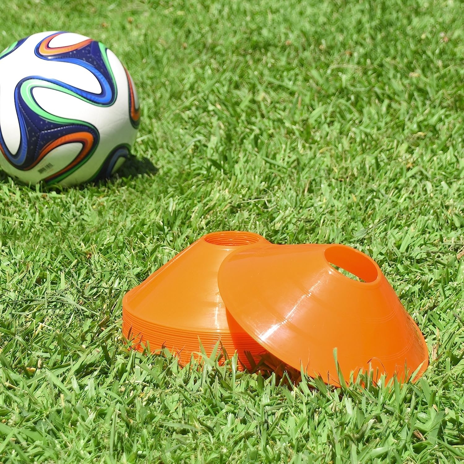 Stack of orange training cones next to soccer ball on grass