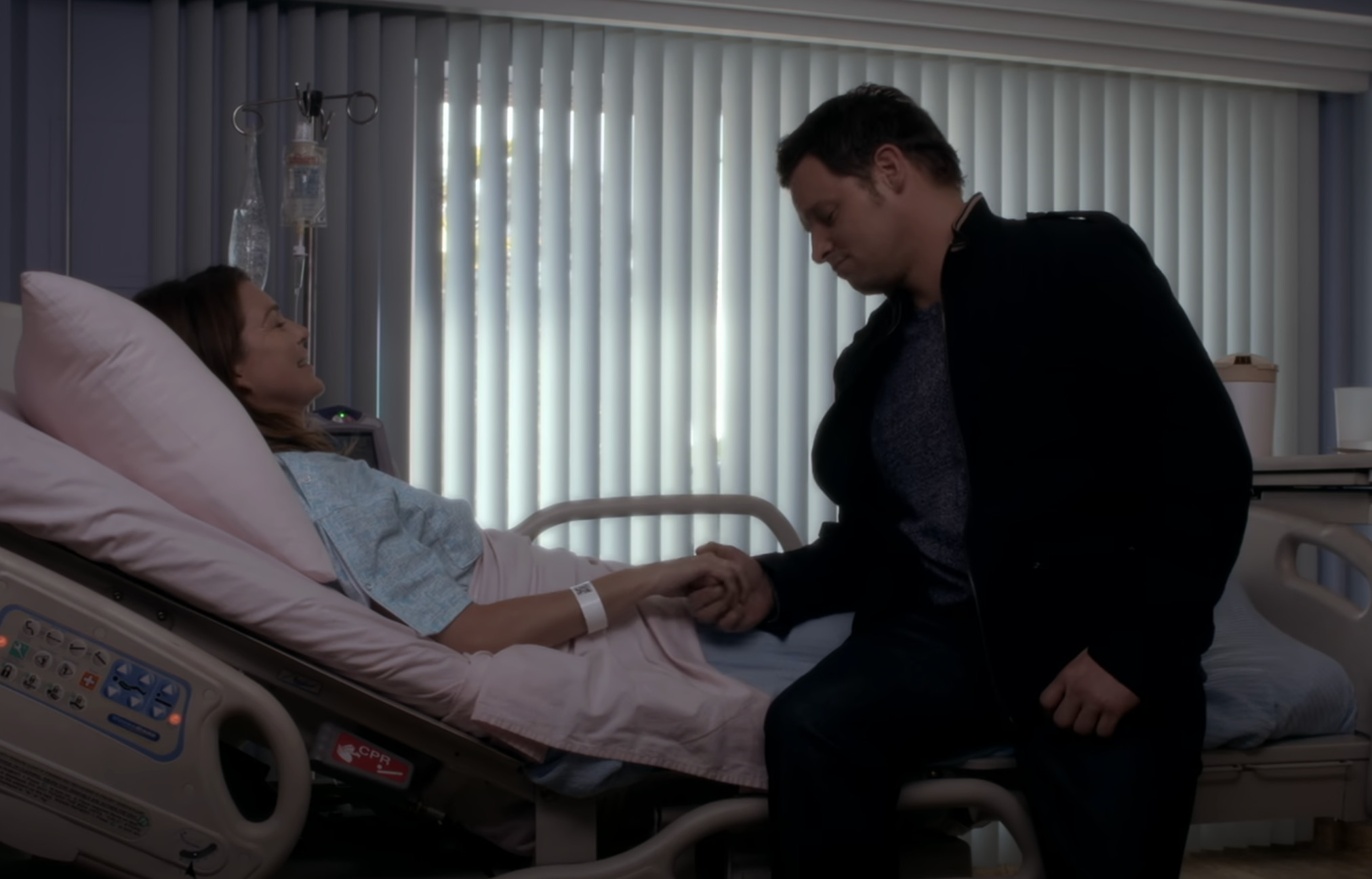 Meredith and Alex holding hands in the hospital bed after she gives birth