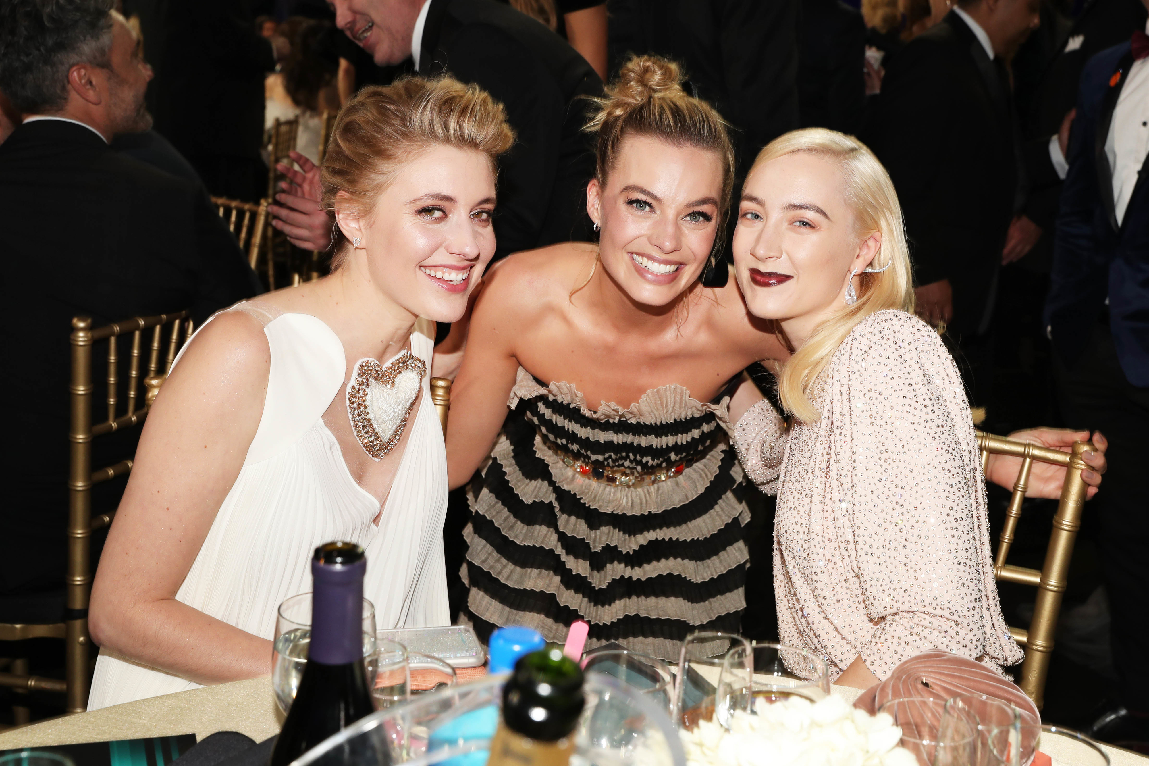 Greta, Margot, and Saoirse smile for a photo as they sit at a dinner table during an awards show