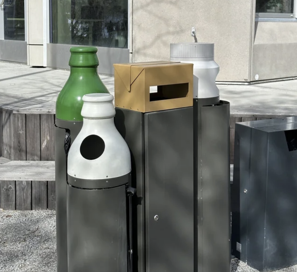 The tops of the recycling bins are decorated with a glass bottle, plastic cup, and cardboard box to indicate which items go in which bin