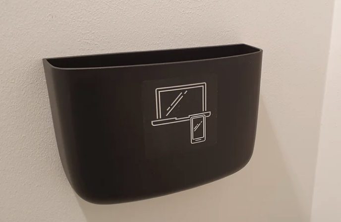 The large bin is attached to a wall and has pictures of a laptop and cellphone drawn on it