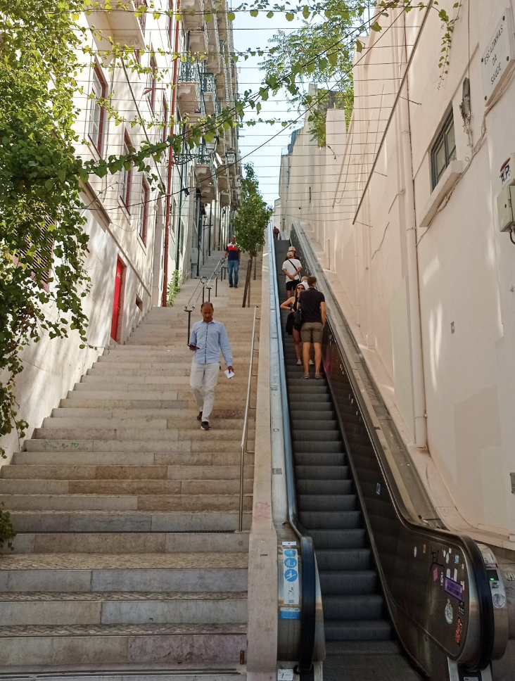 A stairway and escalator run up a hill to connect two outdoor streets