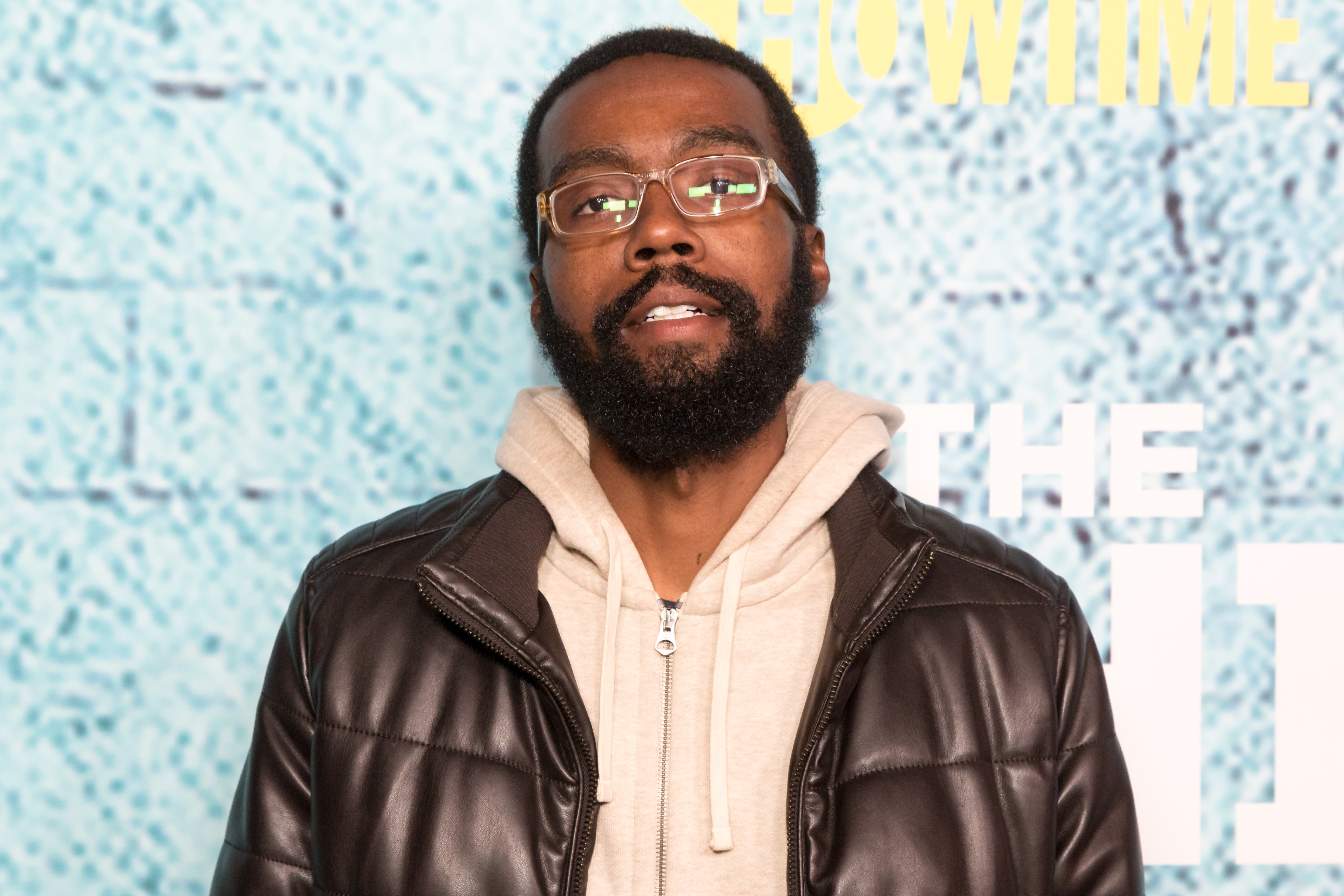 Corey Hendrix at the premiere of The Chi wearing a dark jacket and hoodie underneath with a pair of clear glasses