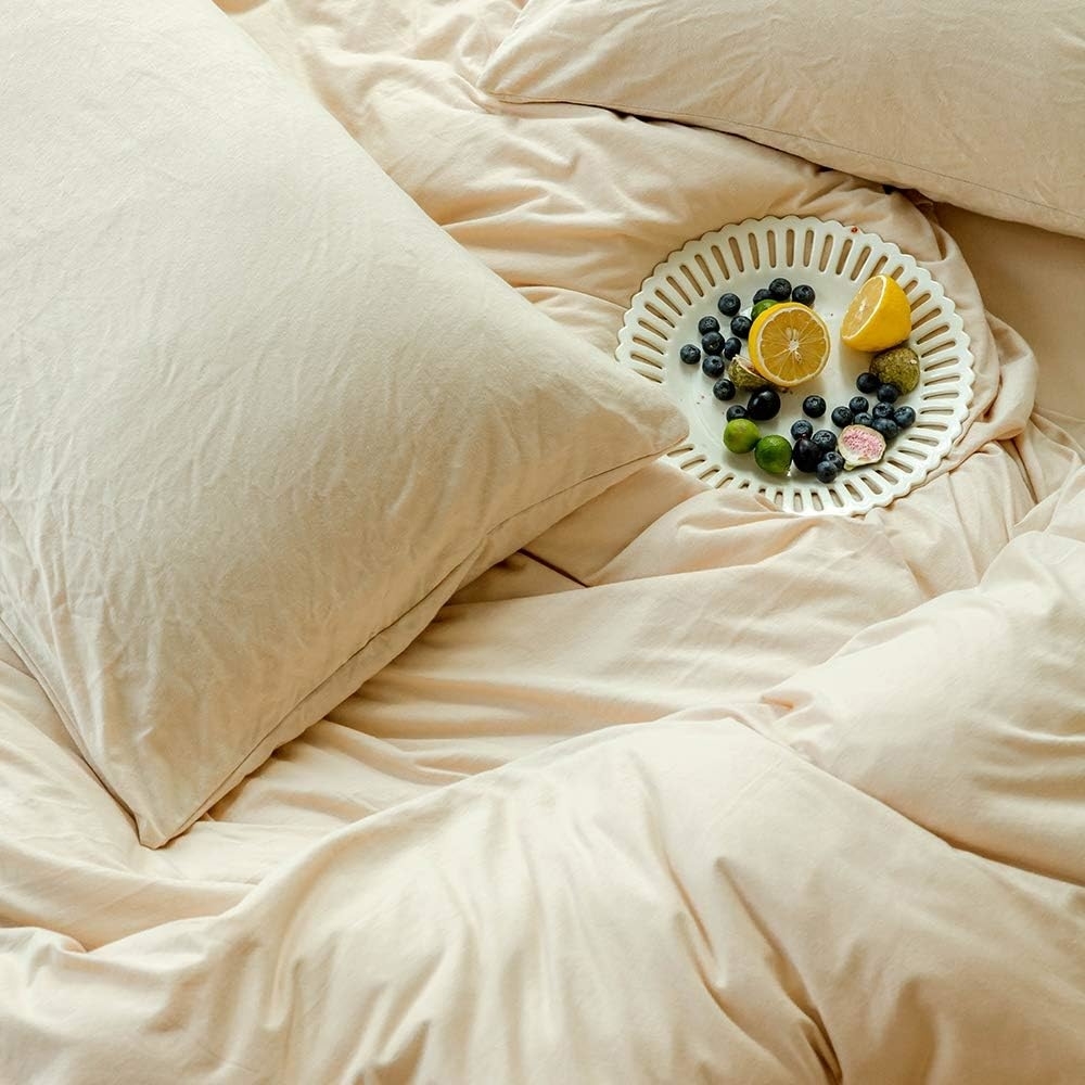 unmade bed with plate of fruit on pillow