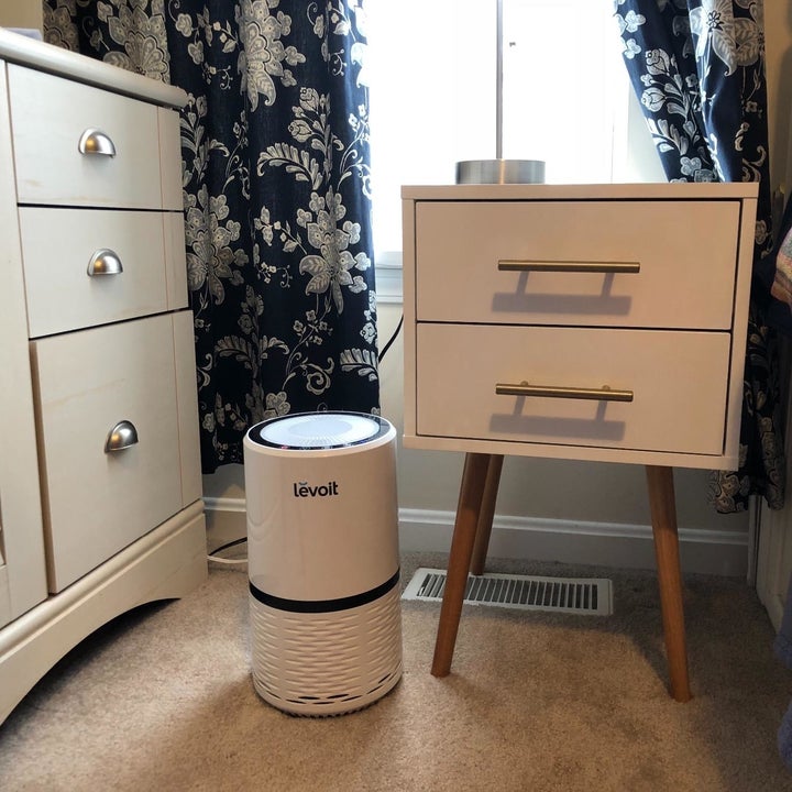 The air purifier in white sitting next to a nightstand