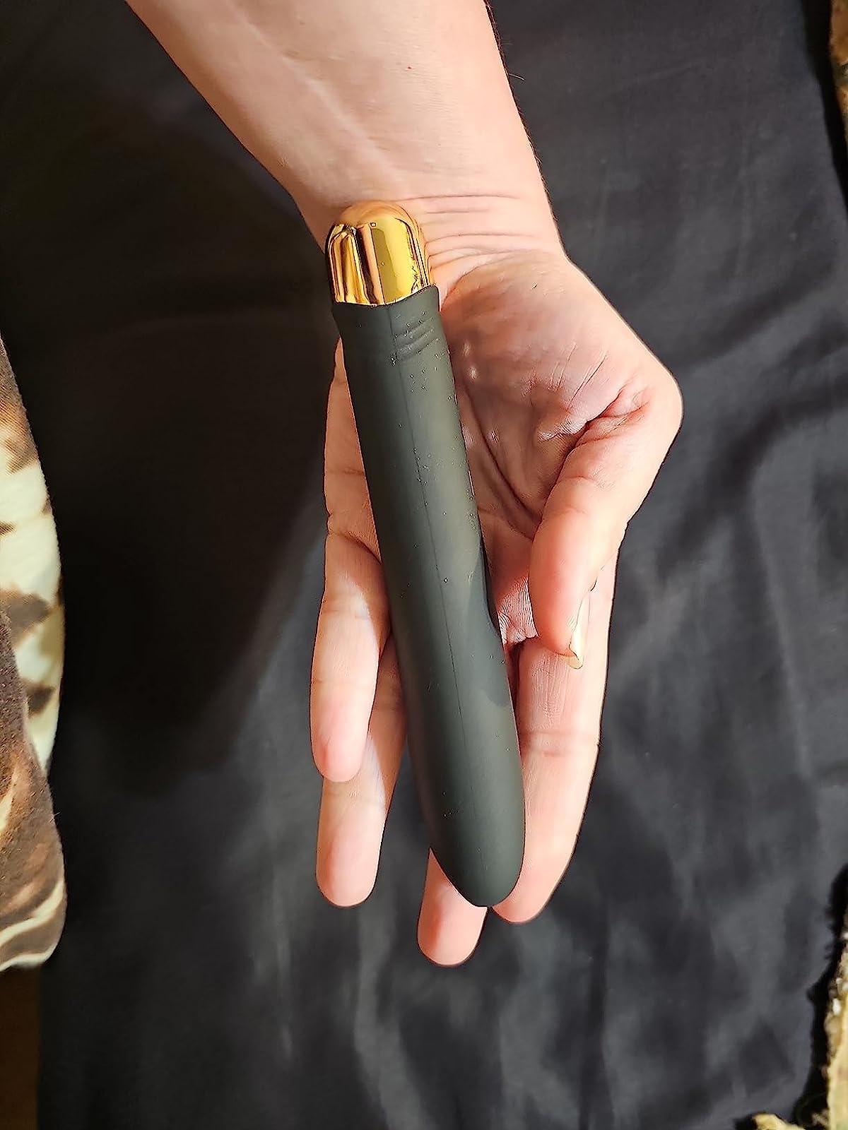 Reviewer holding slim black bullet vibrator with green accent