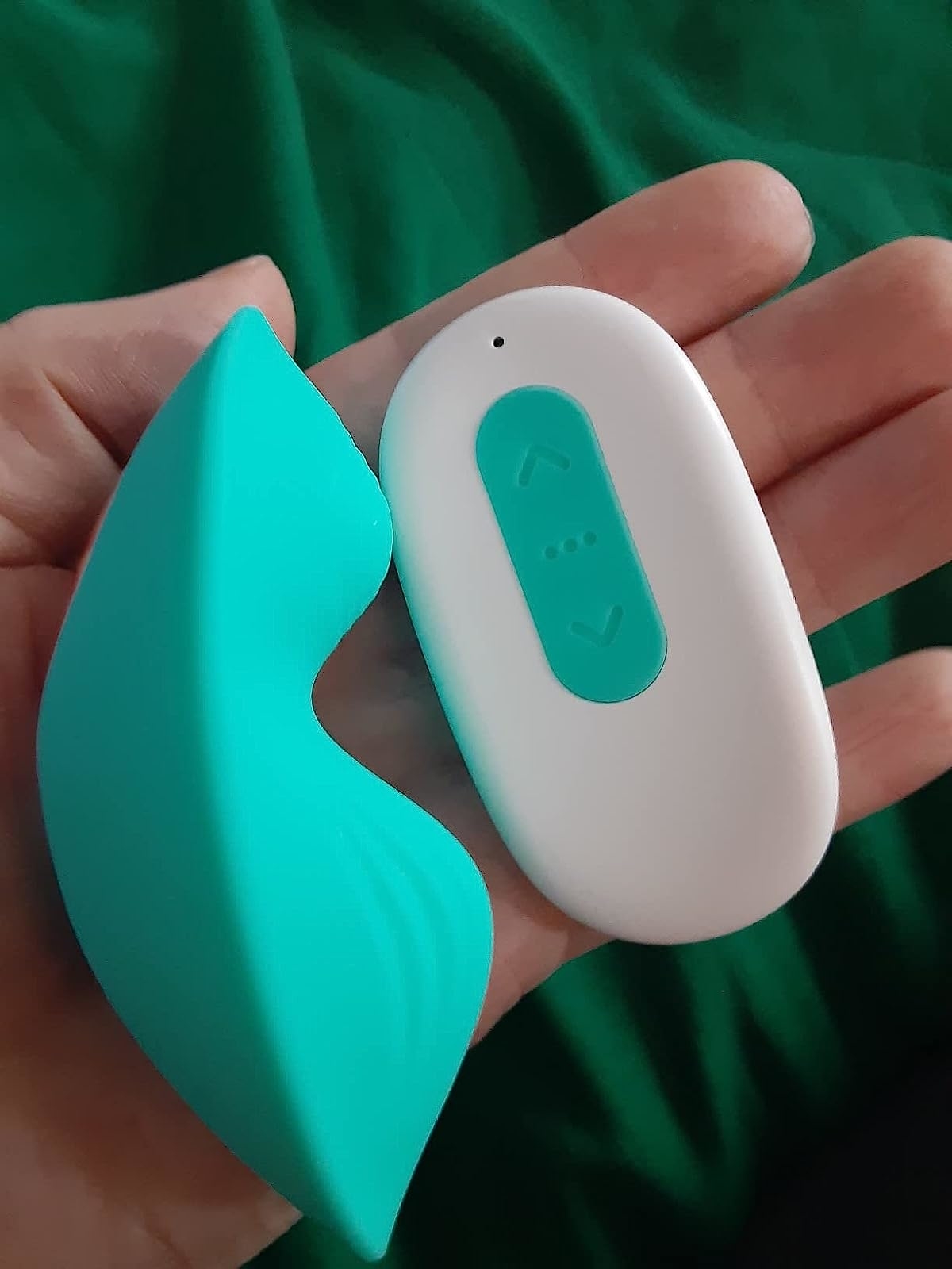 Reviewer&#x27;s hand holding green panty vibrator and white wireless remote