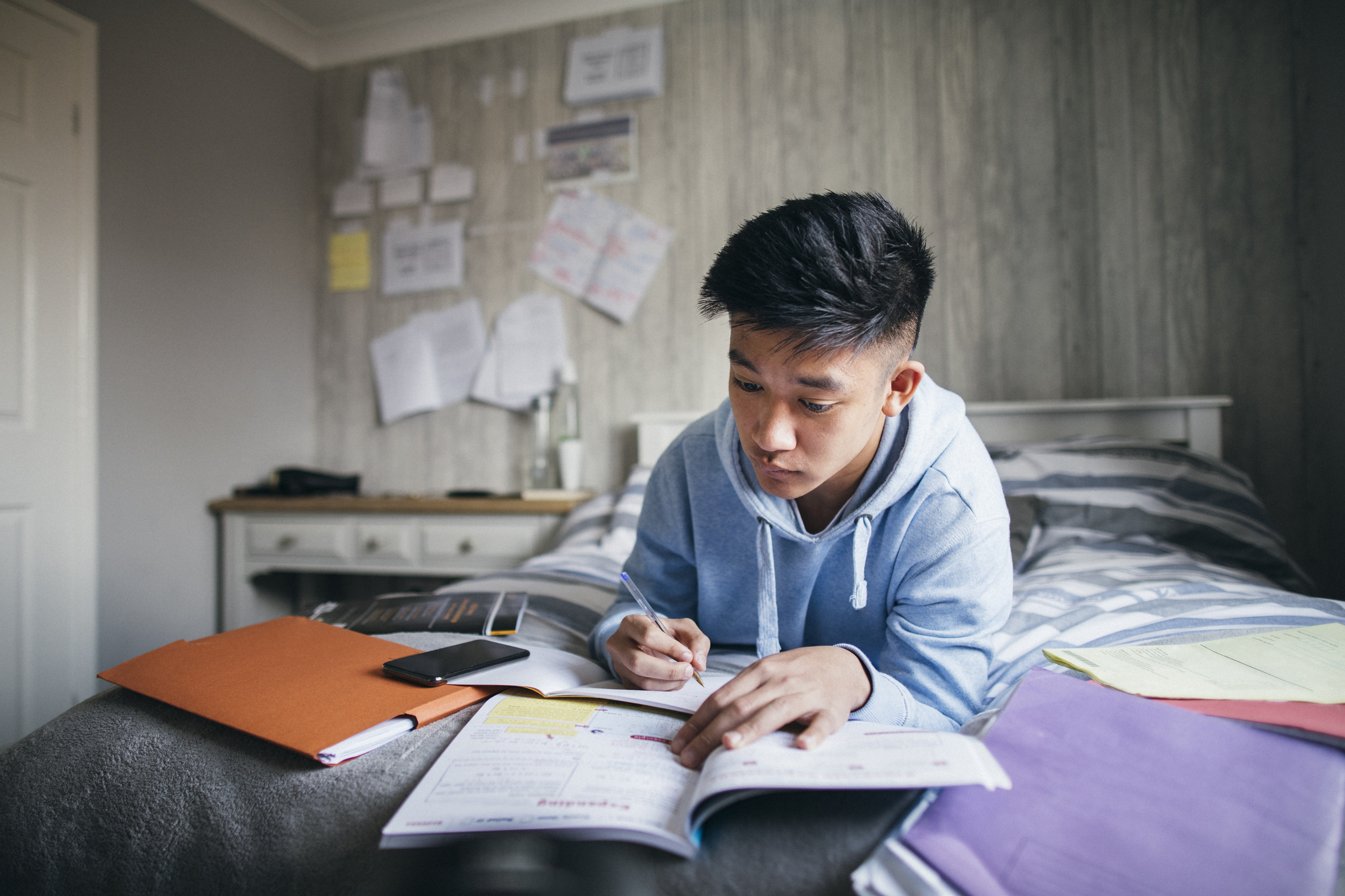 teen doing homework on his bed