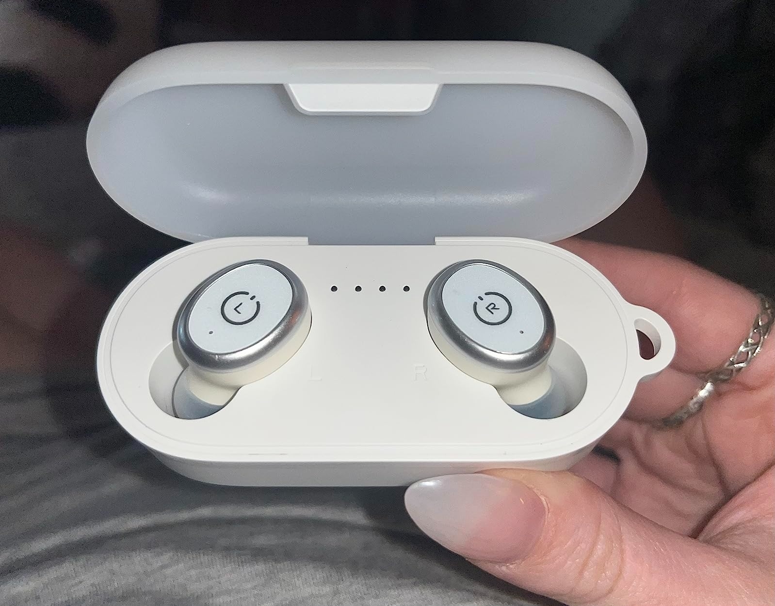 image of reviewer holding up white earbuds in their matching charging case