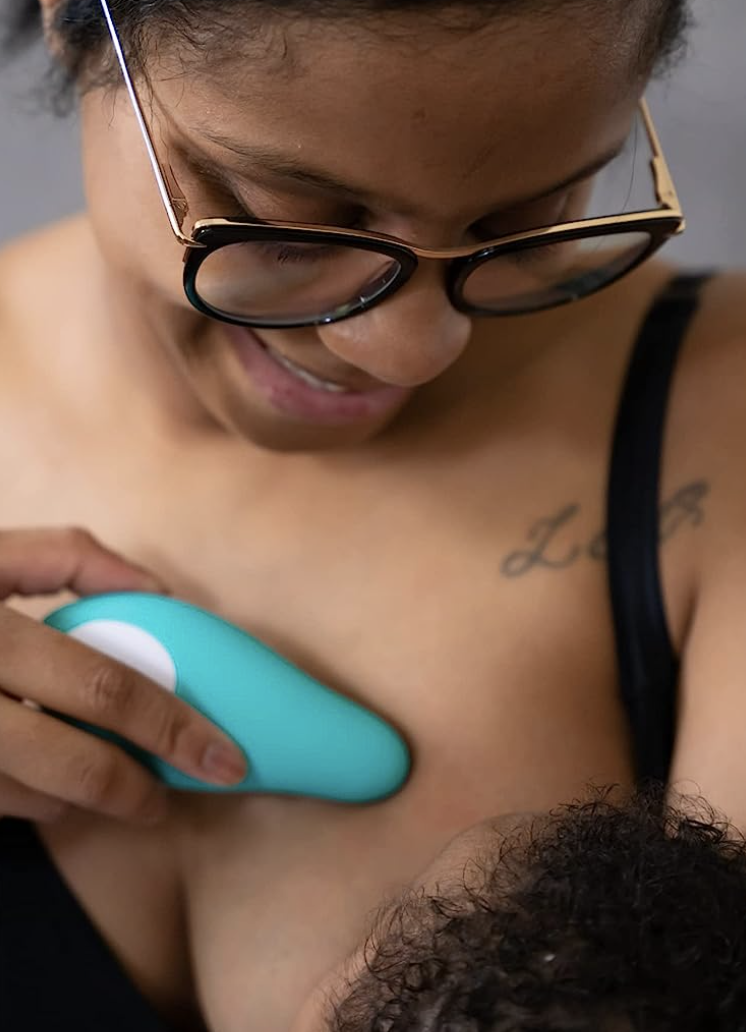parent nursing child while holding massager against breast