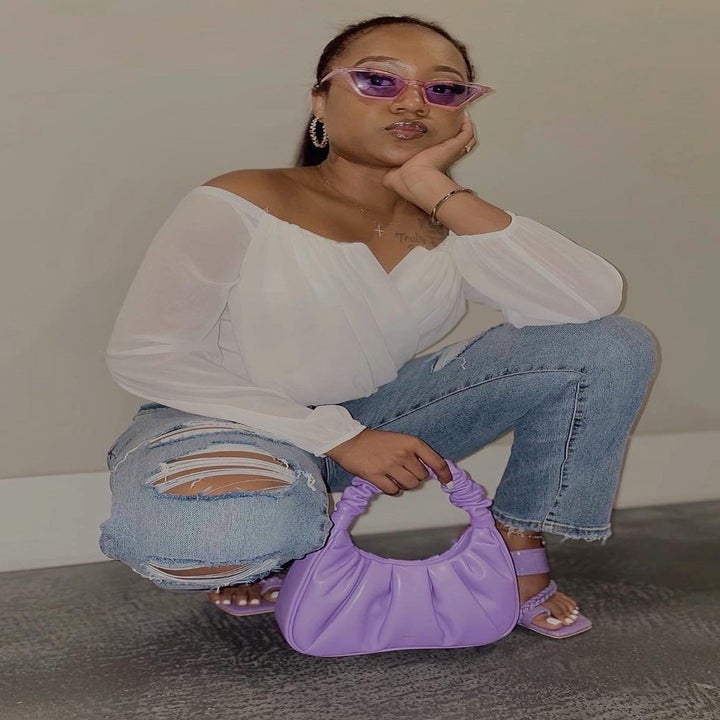 reviewer wearing the bag in purple with matching heels, jeans, and a white top