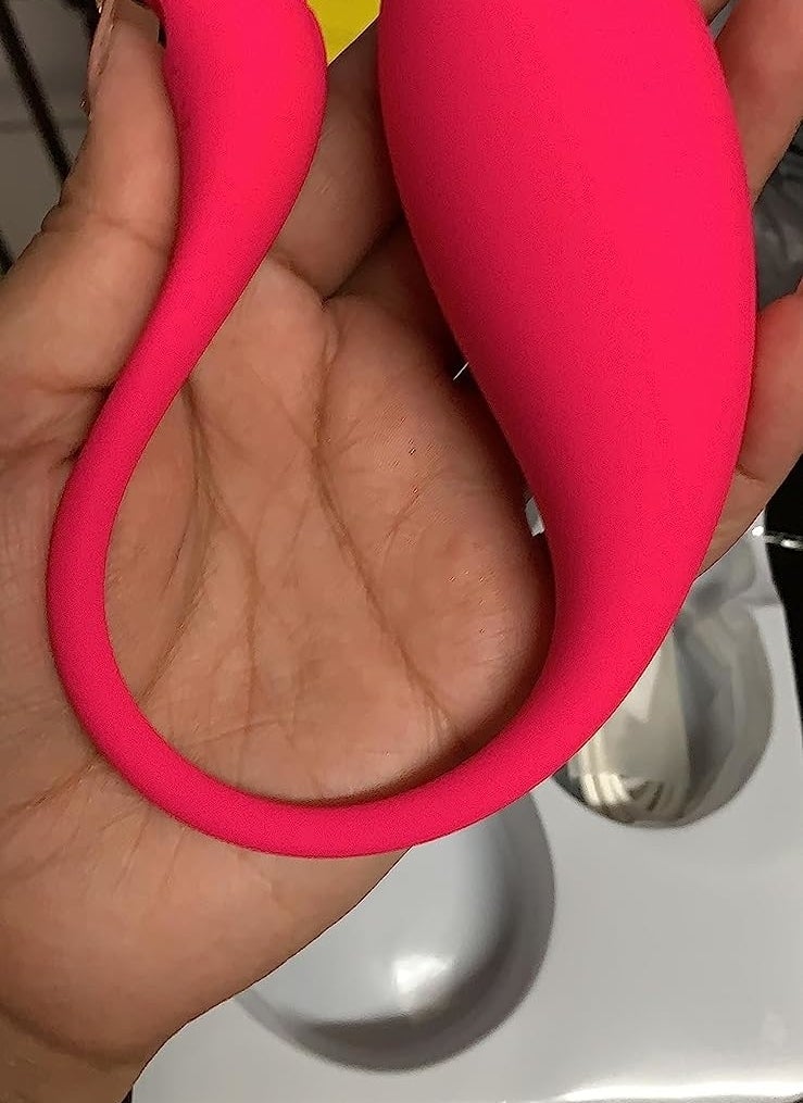 Hand holding pink dual-stimulating wearable vibrator