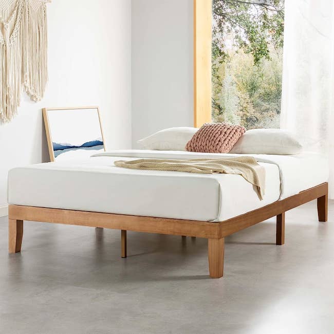 wood bed frame with mattress and blanket on top