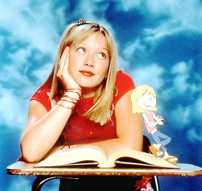 Hilary Duff as Lizzie McGuire sitting at a school desk with an open book daydreaming as the illustrated Lizzie leaning against her