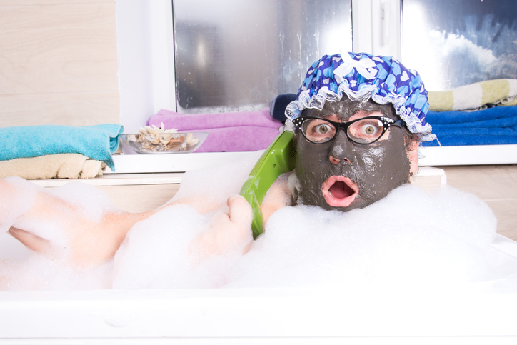 person with a mud face mask in shock on the phone during a bubble bath