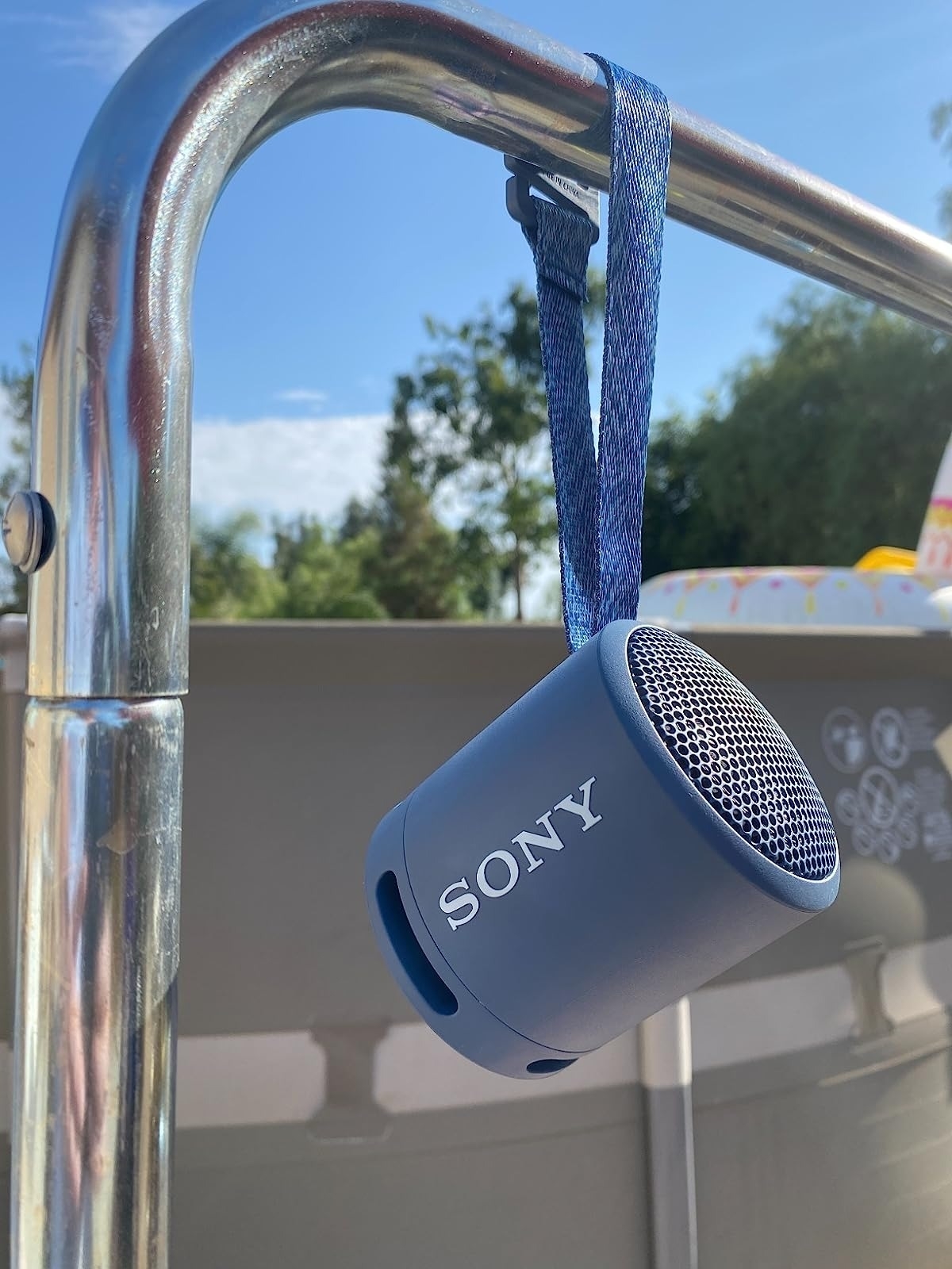 reviewer image of the light blue speaker hanging from a metal bar by a pool