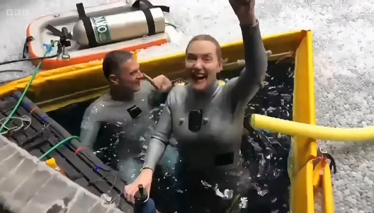 Kate emerging from the water with her hand raised and smiling