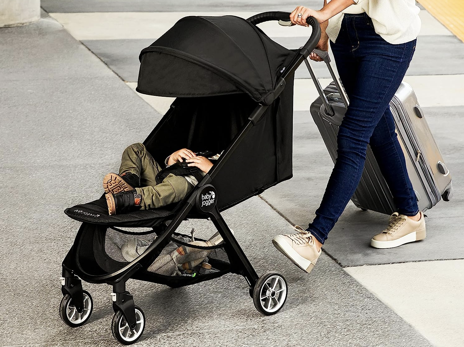 parent pushing child in stroller while pulling suitcase