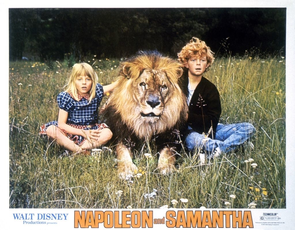 the two kids next to a lion in the field