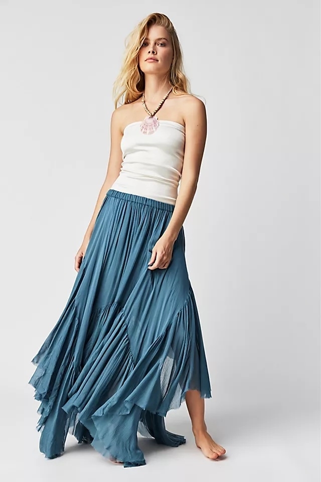 A model wearing a blue skirt with a white top and seashell necklace