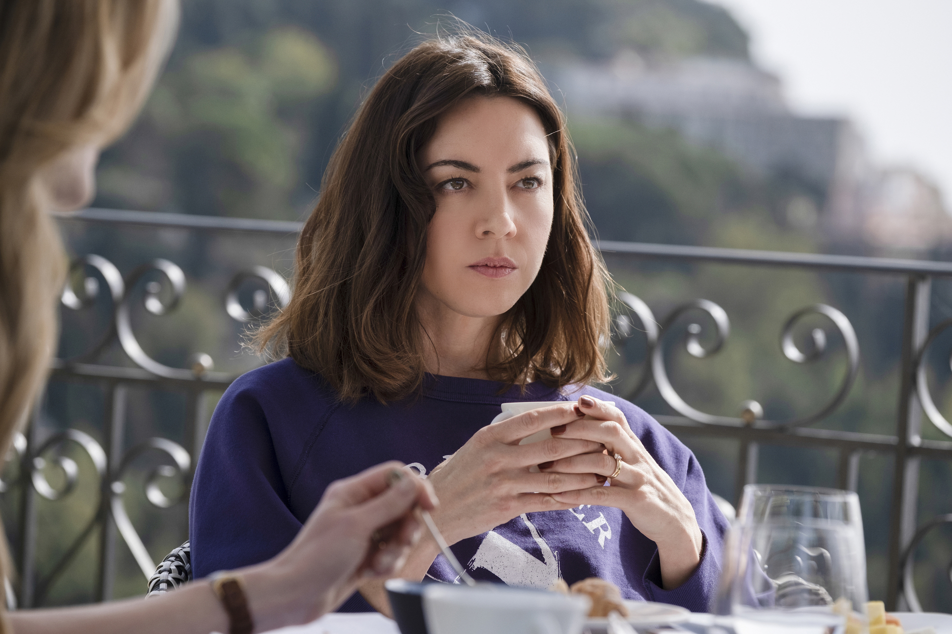 Aubrey Plaza holding a cup of coffee in a scene from The White Lotus