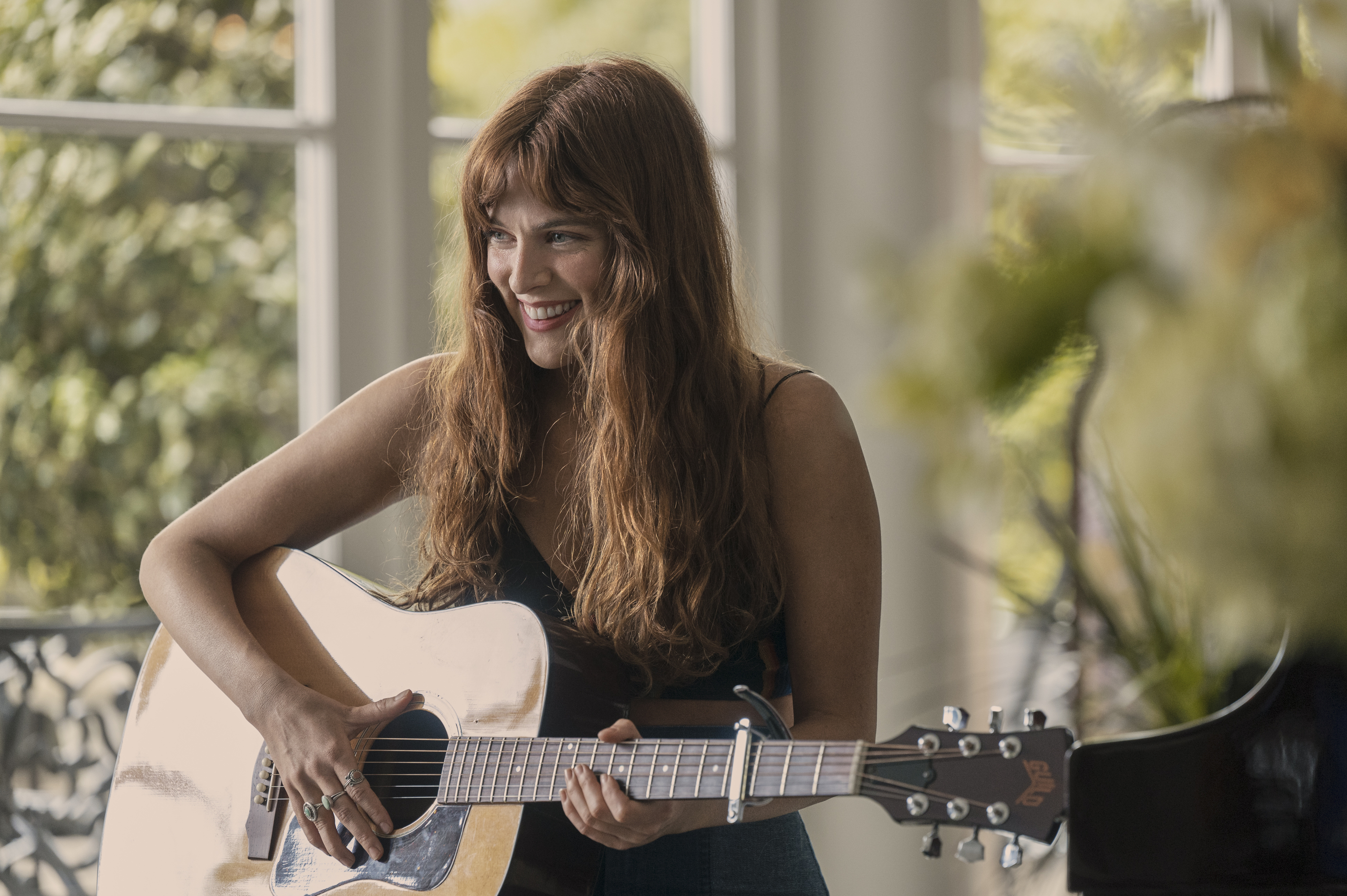 Riley Keough playing the guitar in a scene from Daisy Jones &amp;amp; the Six