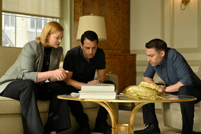 Shiv, Kendall, and Roman Roy sitting around a coffee table in a scene from Succession