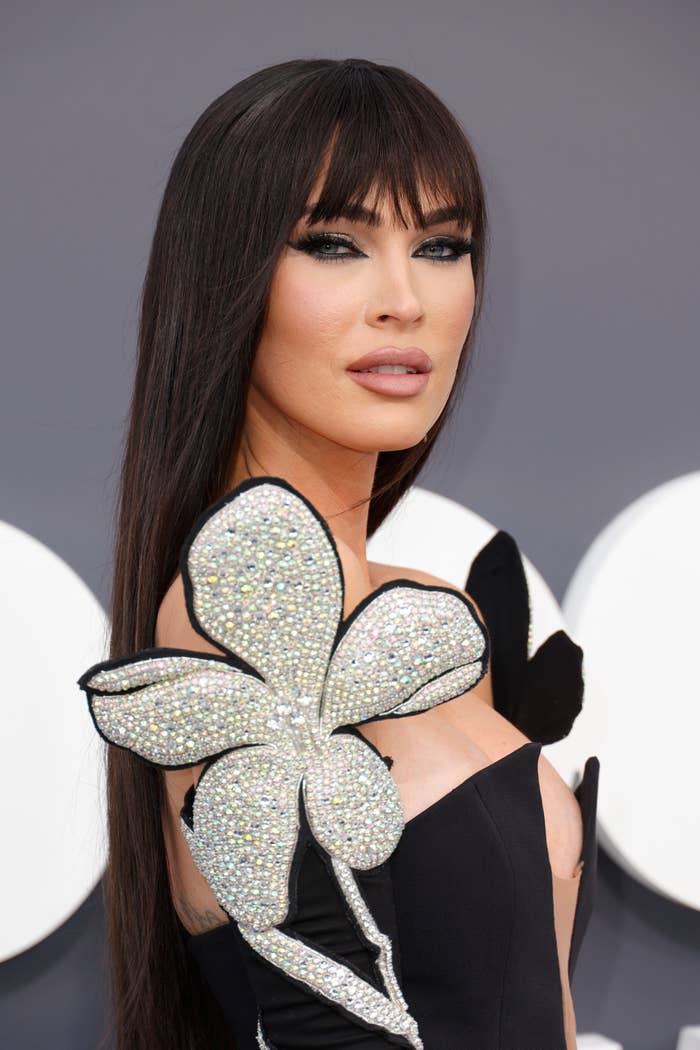 A closeup of Megan Fox on the red carpet wearing an outfit with a large sequined flower on the shoulders