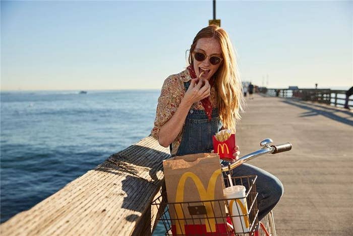 A person sitting on a pier next to their bicycle eating McDonald&#x27;s fries