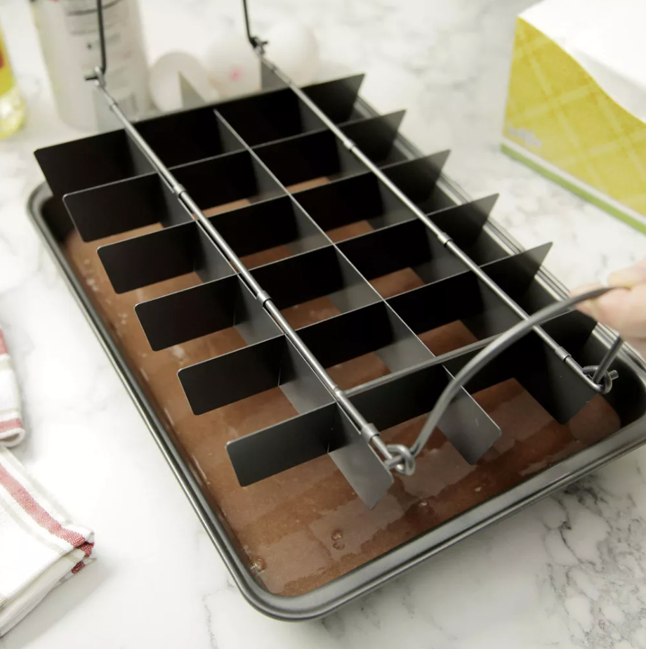 a pan of brownies being cut with a grid-like cutting tool on a countertop