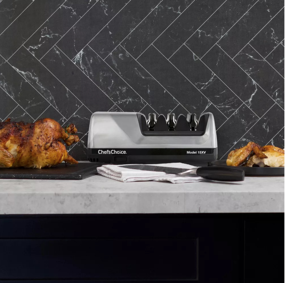 a knife sharpener with three slots on a countertop next to roasted chicken, with a knife sitting in front of the sharpener