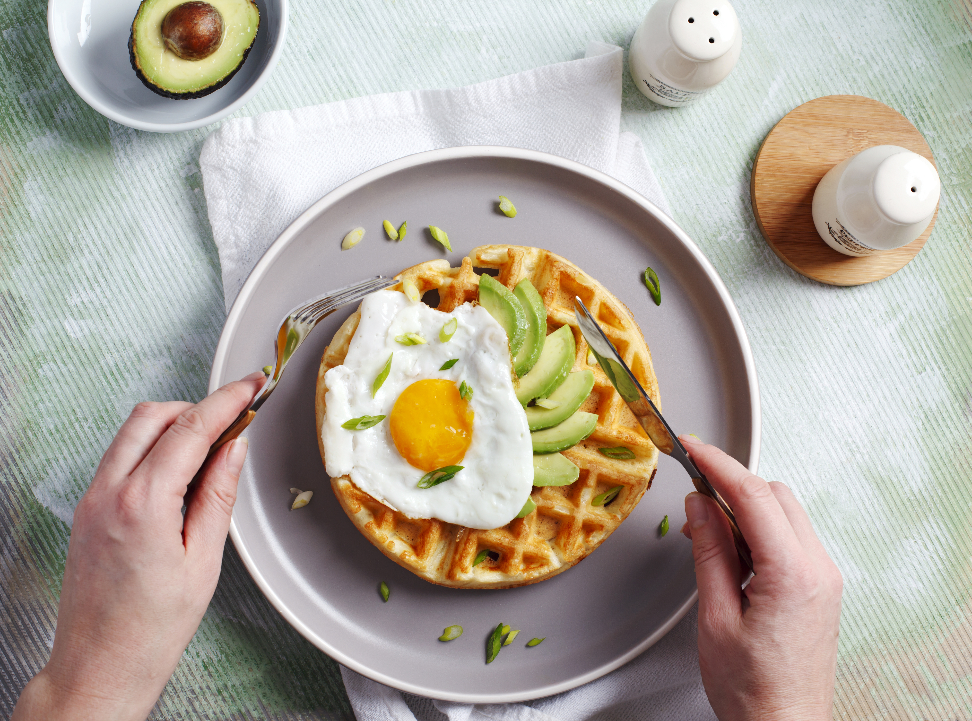 person eating a savory waffle topped with a fried egg and sliced avocado