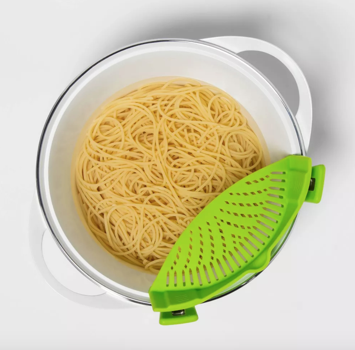 a pot of boiled noodles with a lime-green strainer clipped on to the side