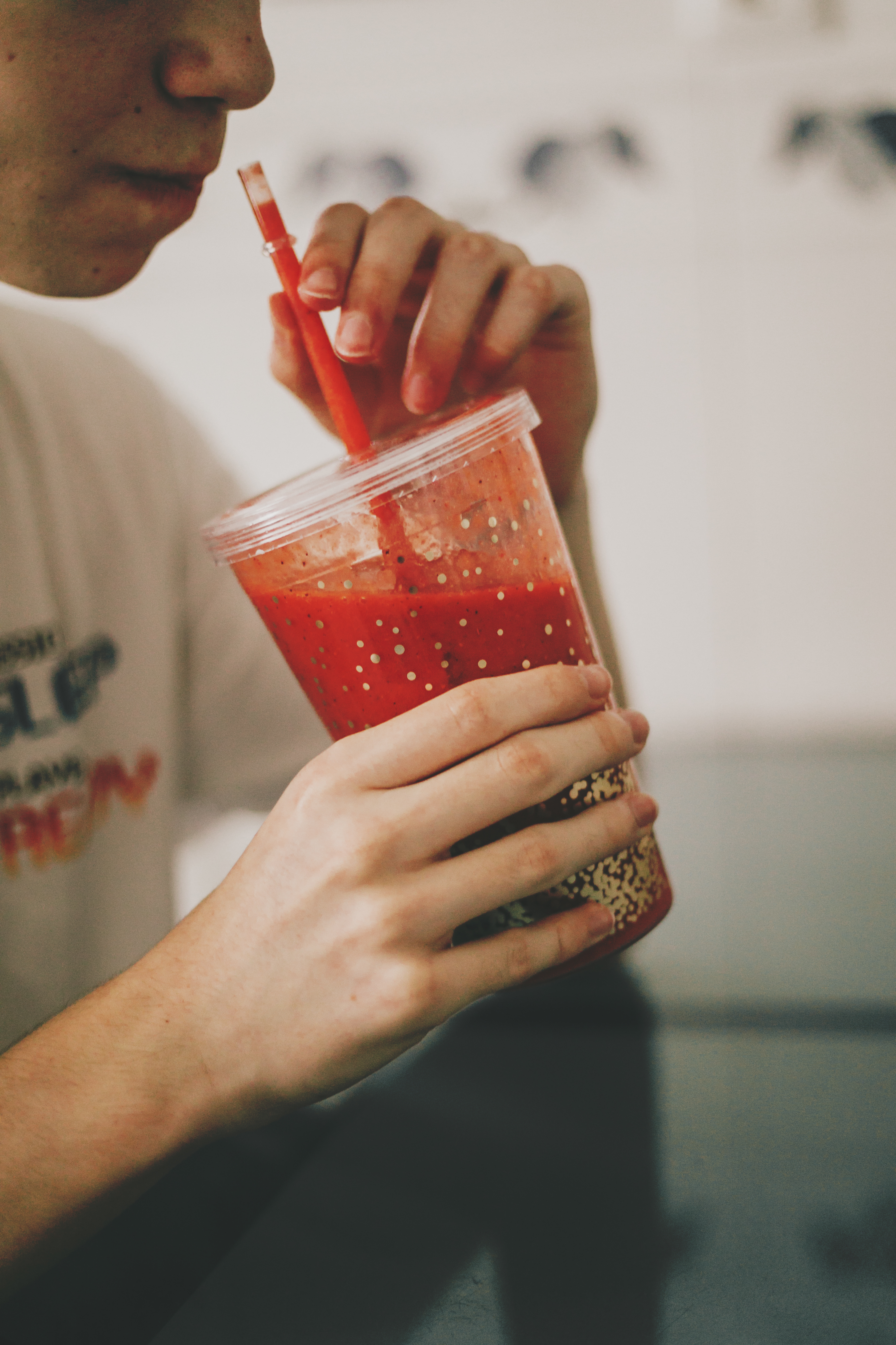 An image of a man holding a drinks tumbler with red liquid and a straw in it.