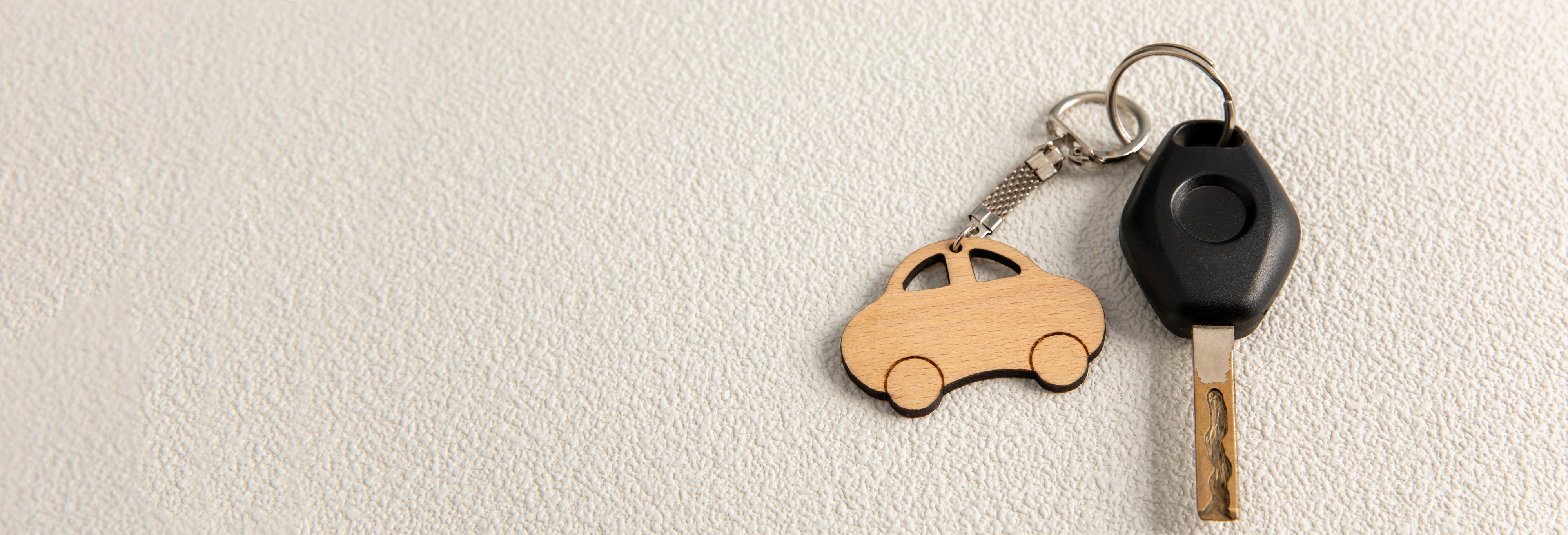 A black car key with a wooden car-shaped key ring on a white textured background.