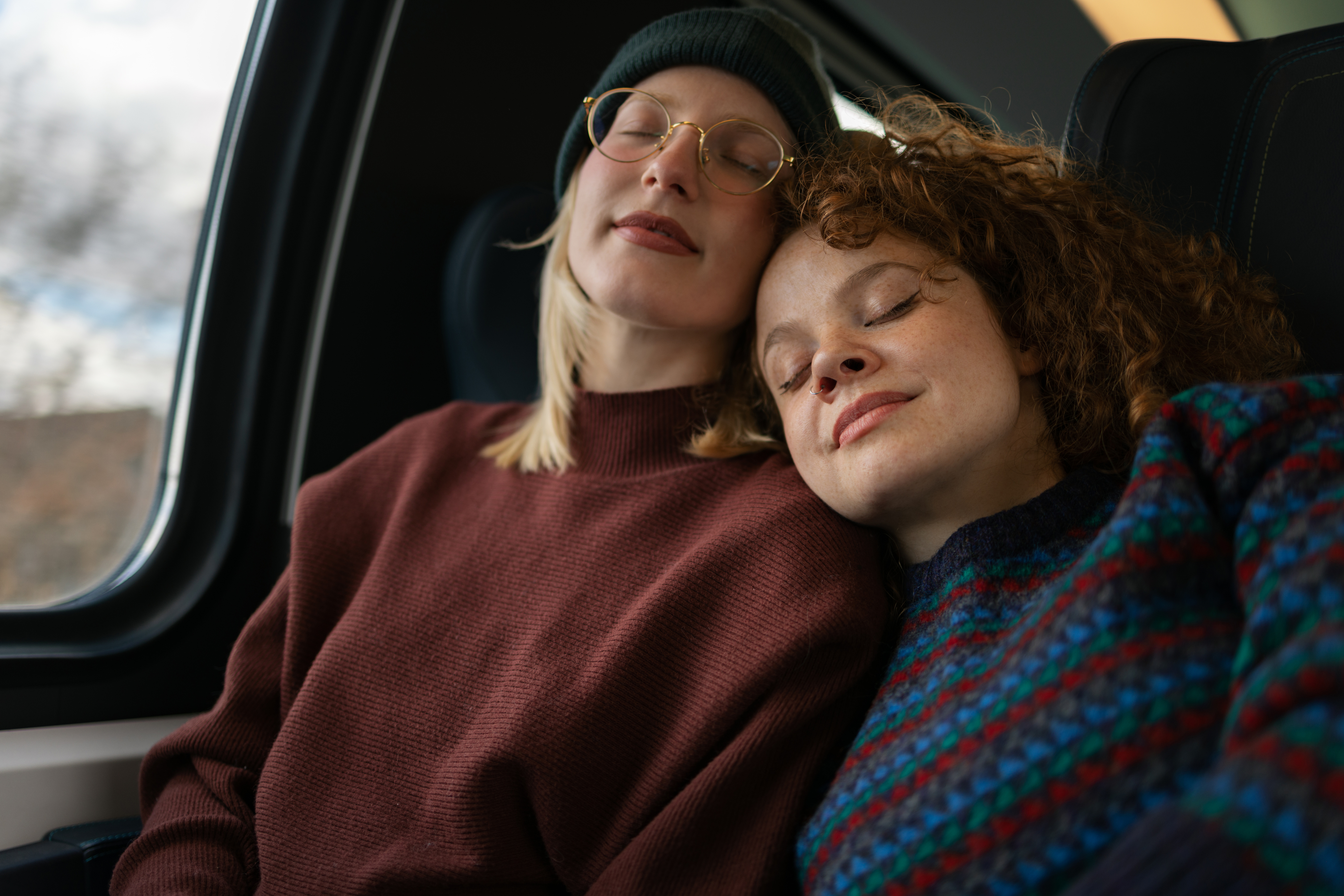 An image of two women sleeping happily in a car, leaning against each other