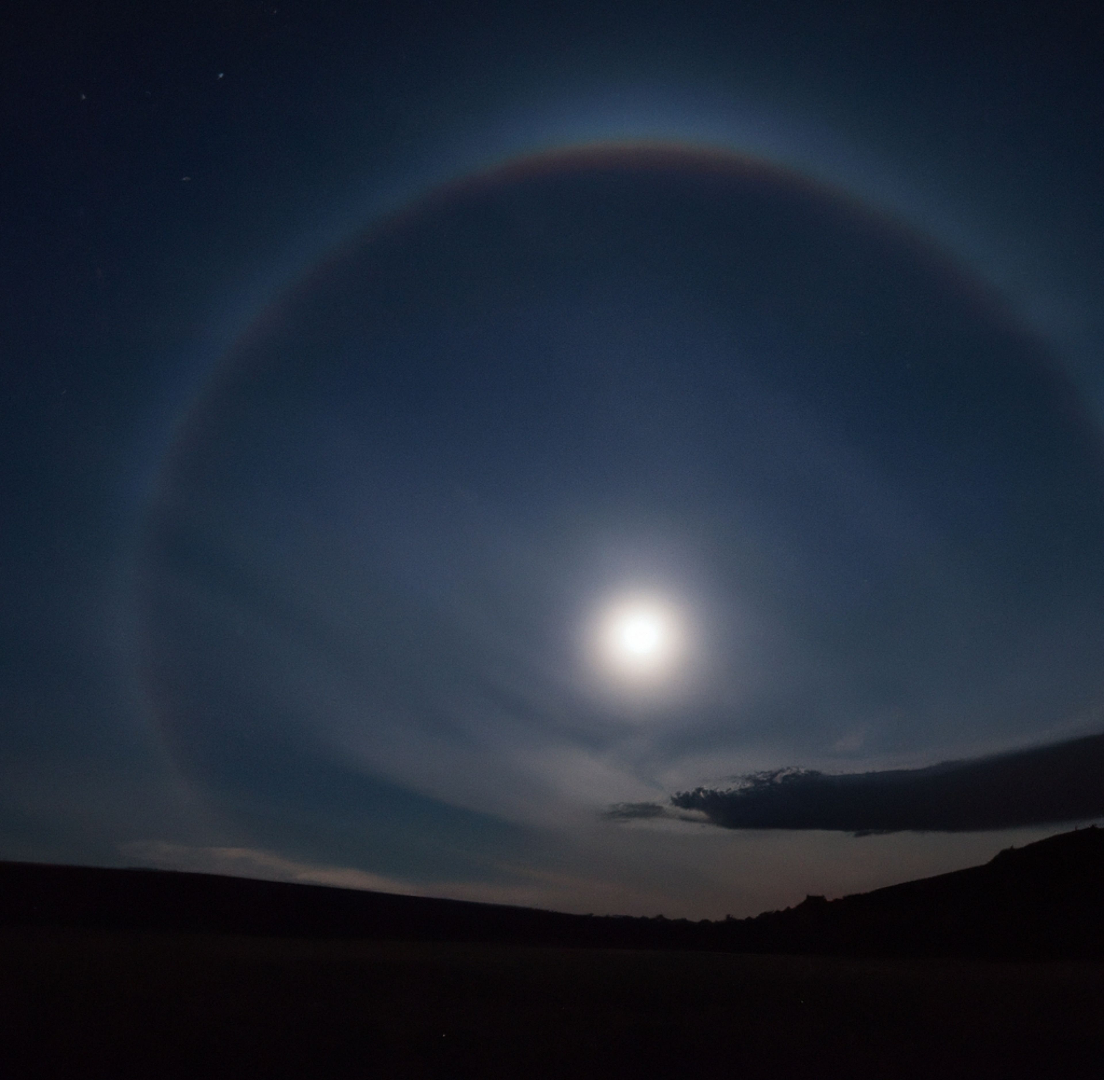 A moonbow in the night sky; it looks like a large white circle around the moon