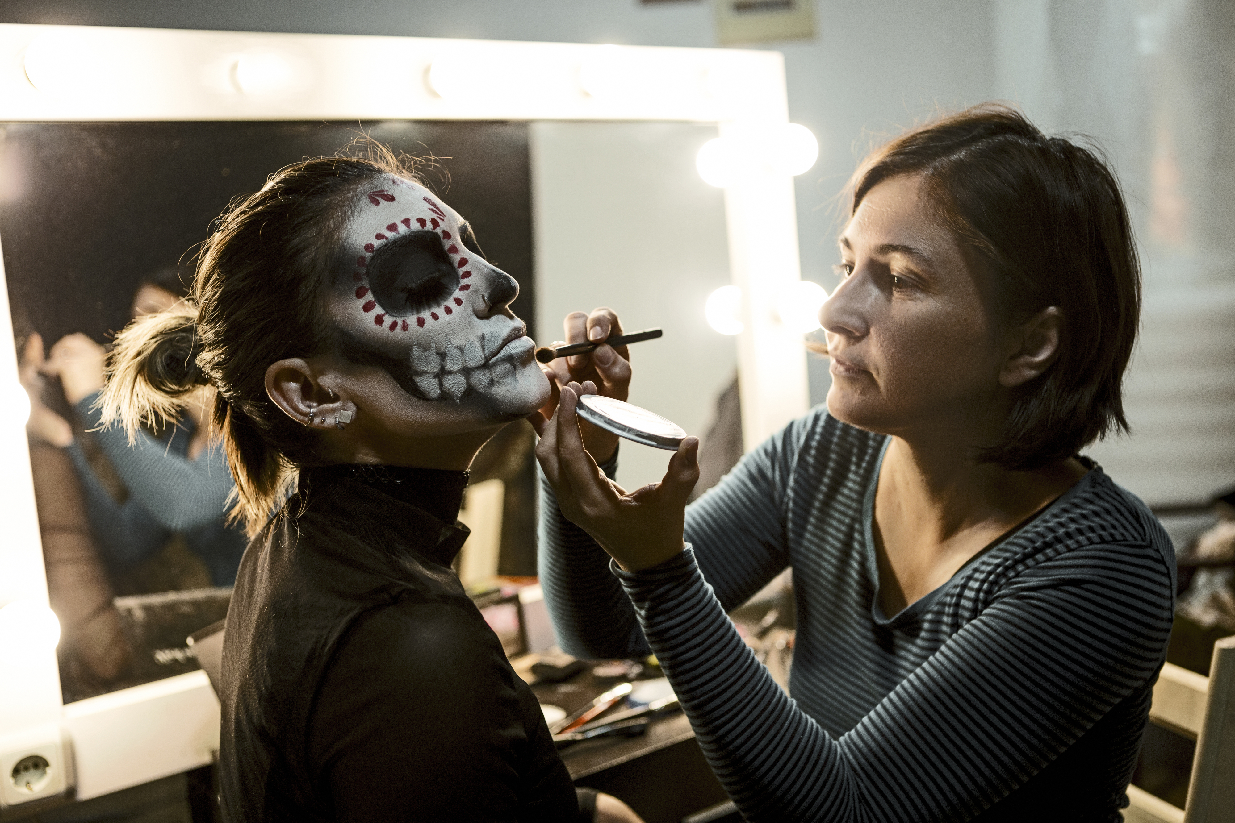 woman painting another woman&#x27;s face for a theater production