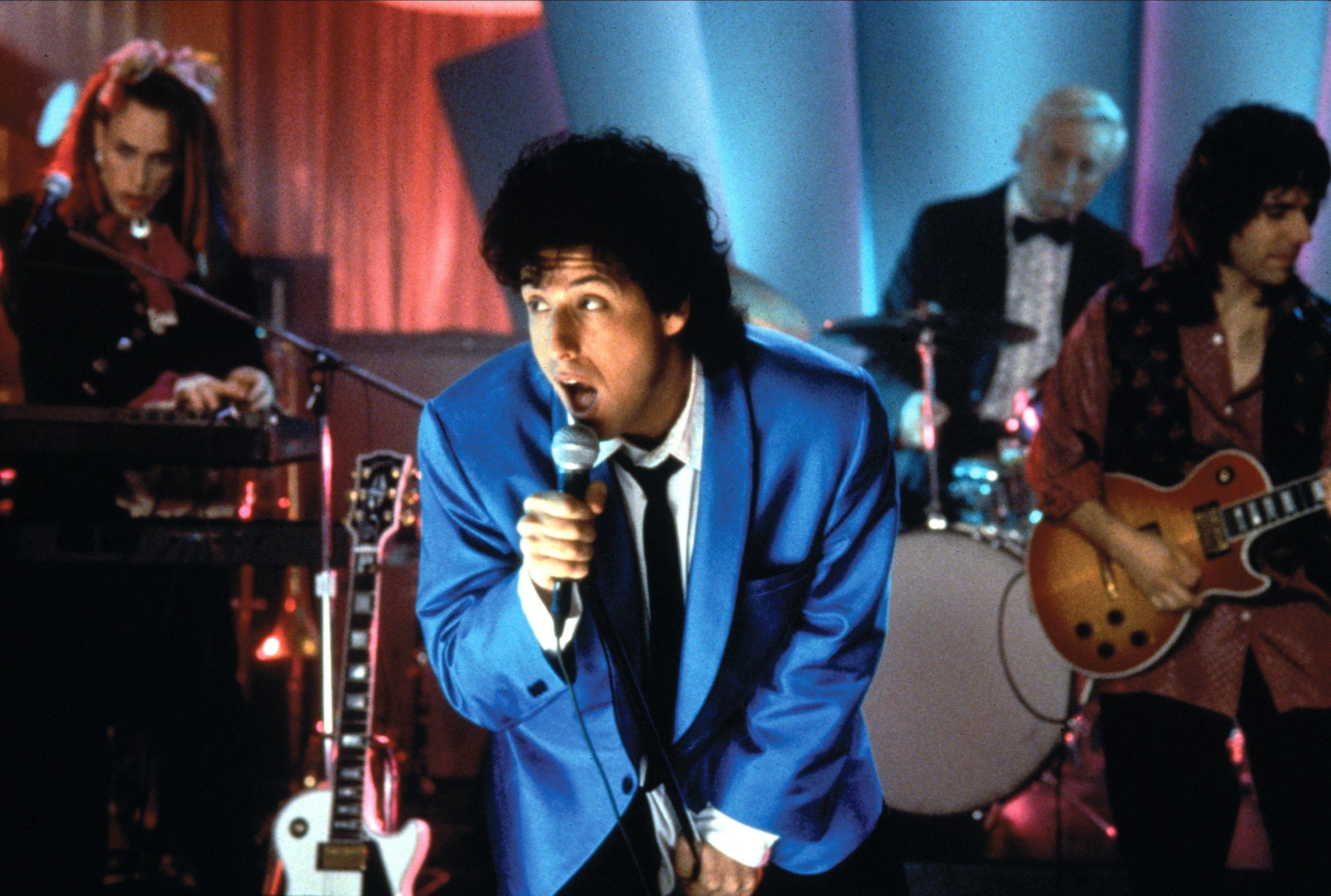 Adam Sandler on stage in a suit and performing in The Wedding Singer
