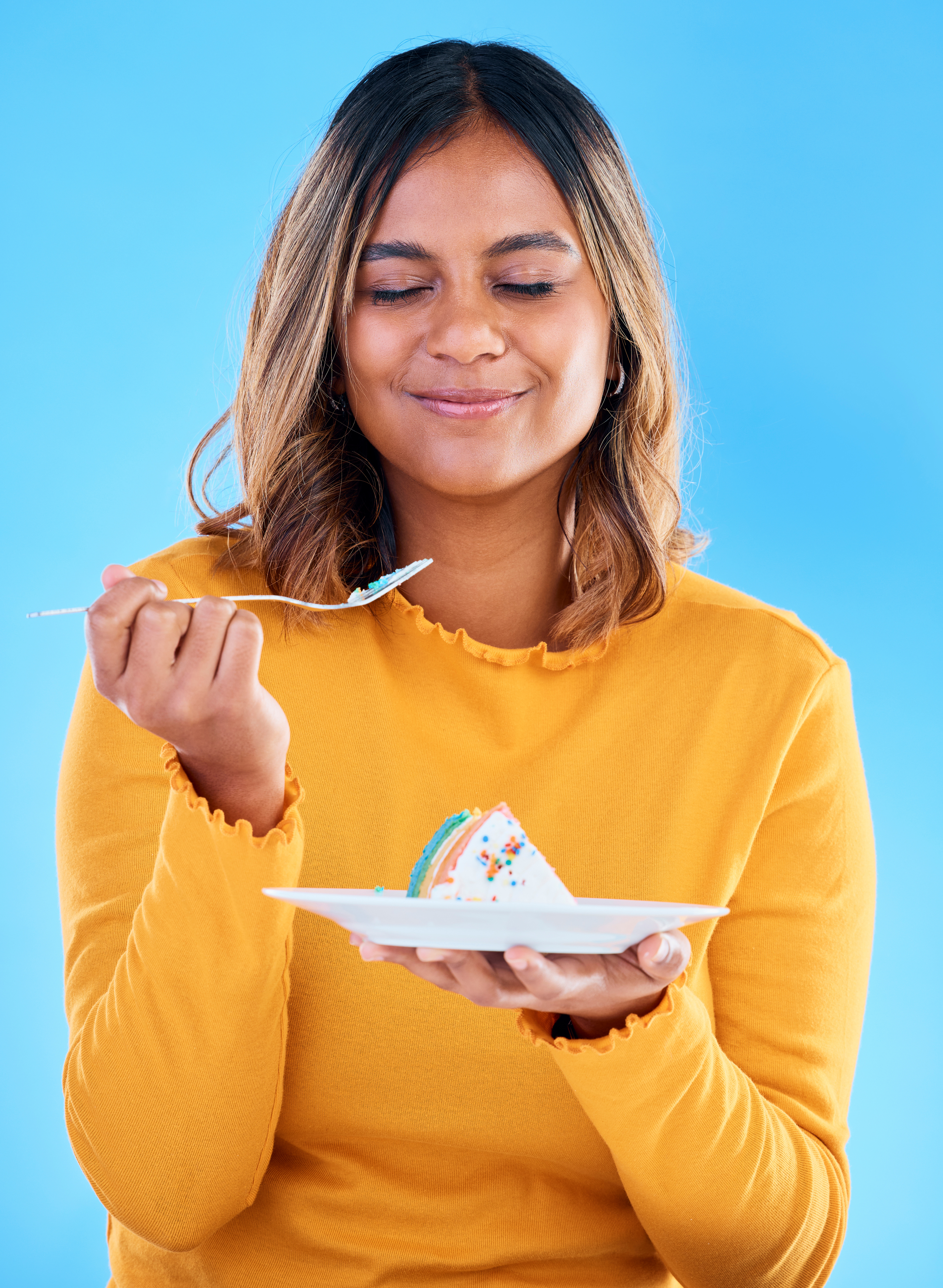 A woman in a yellow long-sleeved T-shirt enjoying a slice of cake