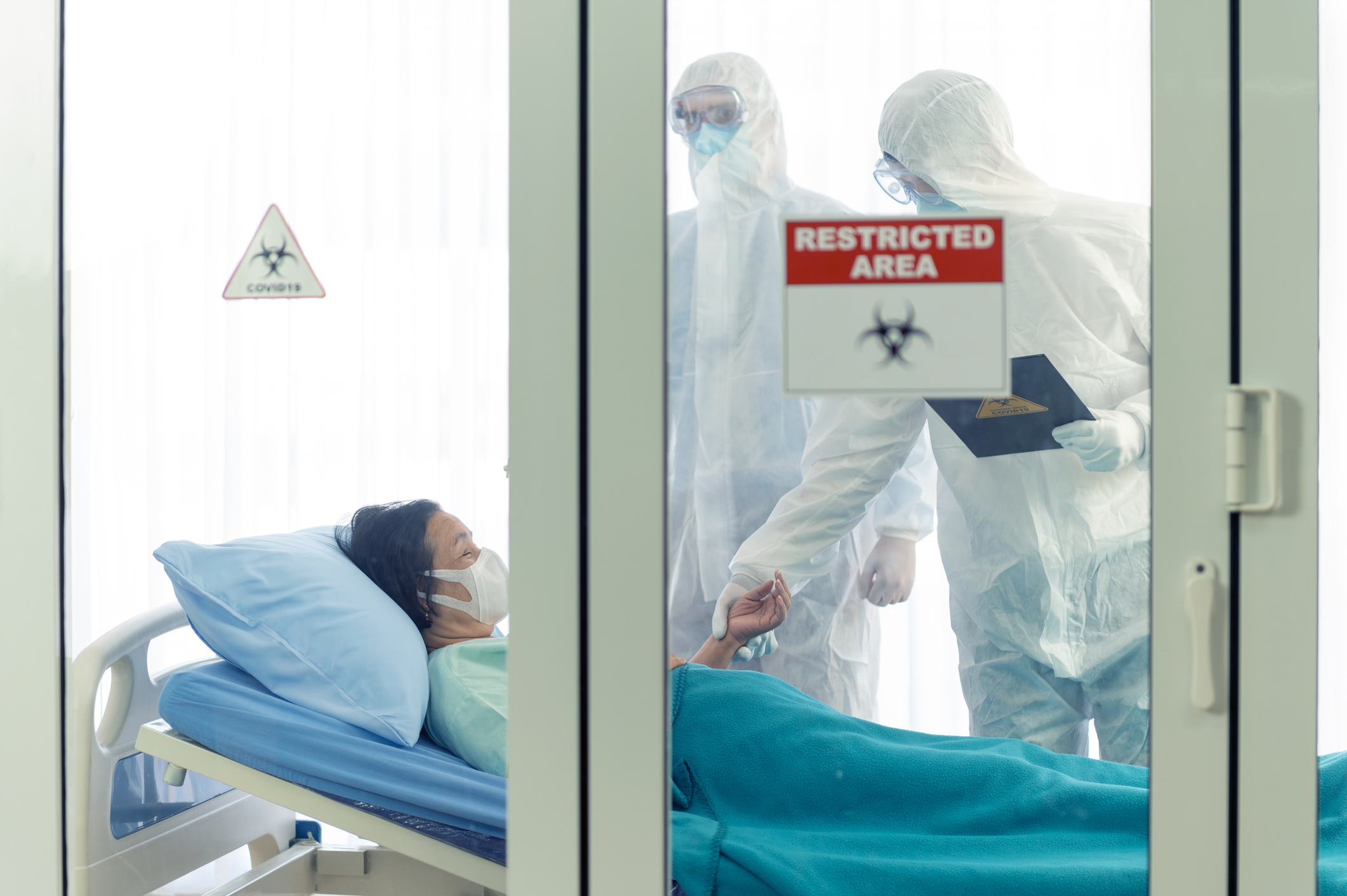woman in a private hospital area with nurses wearing hazmat suits