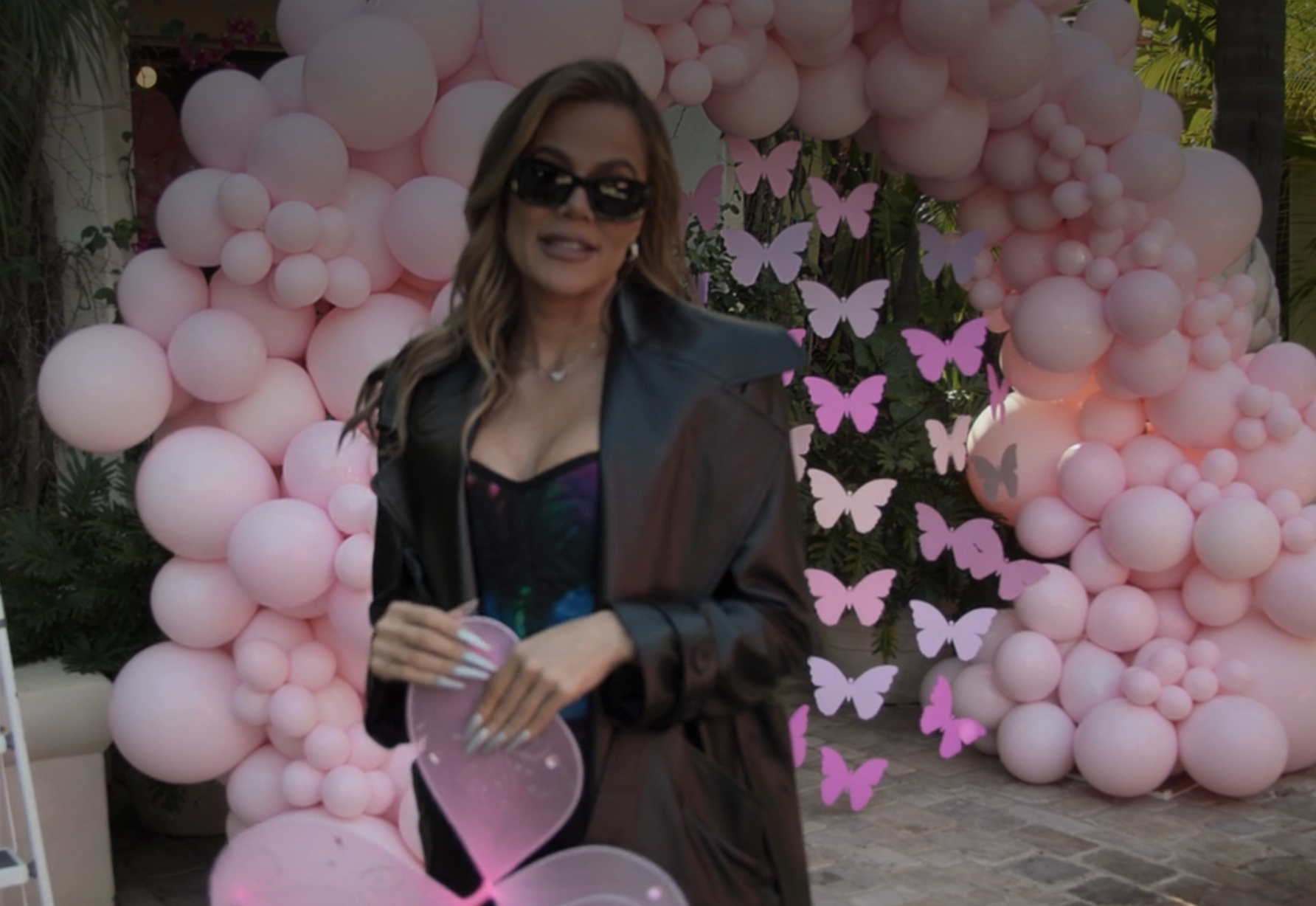 Khloé with a bunch of balloons and butterfly decorations behind her
