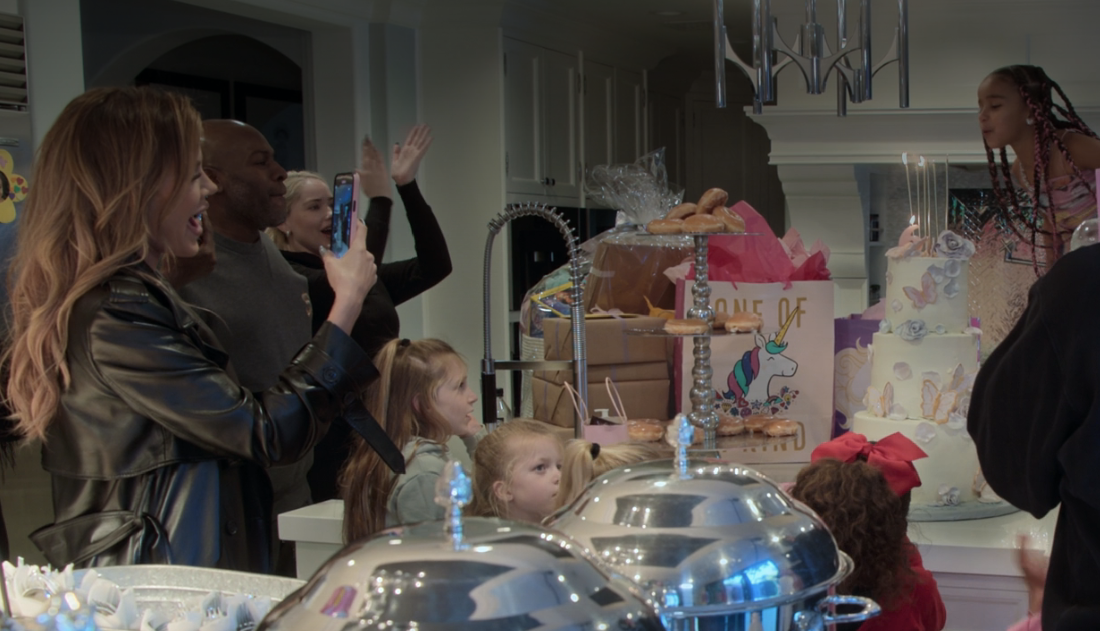 Khloé with other adults and children in a room with a cake and gifts