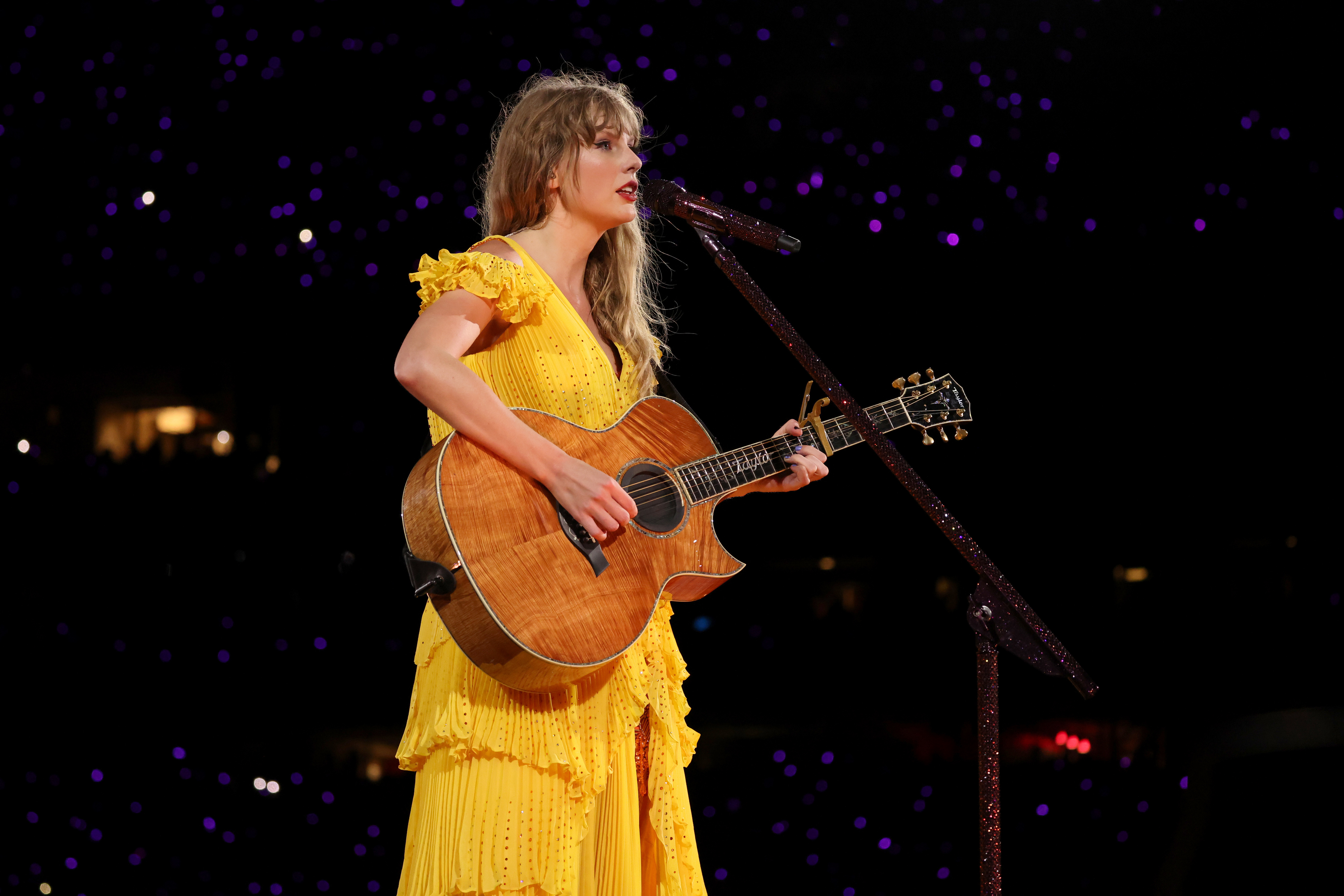 Taylor Swift performing during The Eras Tour in a yellow dress