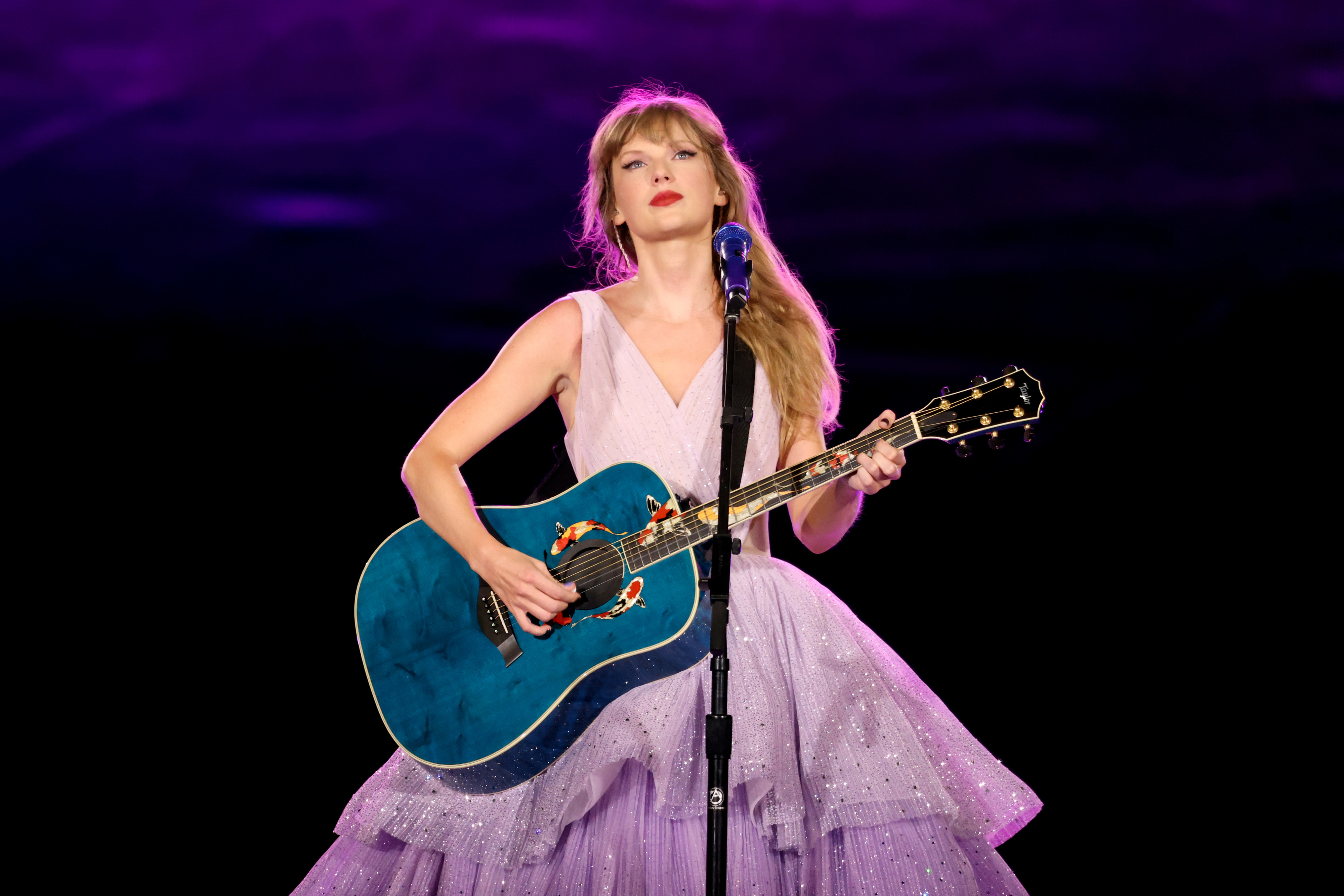 Taylor Swift in a purple dress with a blue guitar during The Eras Tour