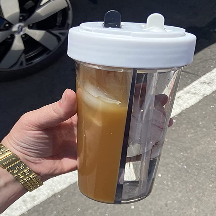 reviewer holding the creative water cup, which is filled with iced coffee on one side and water on the other