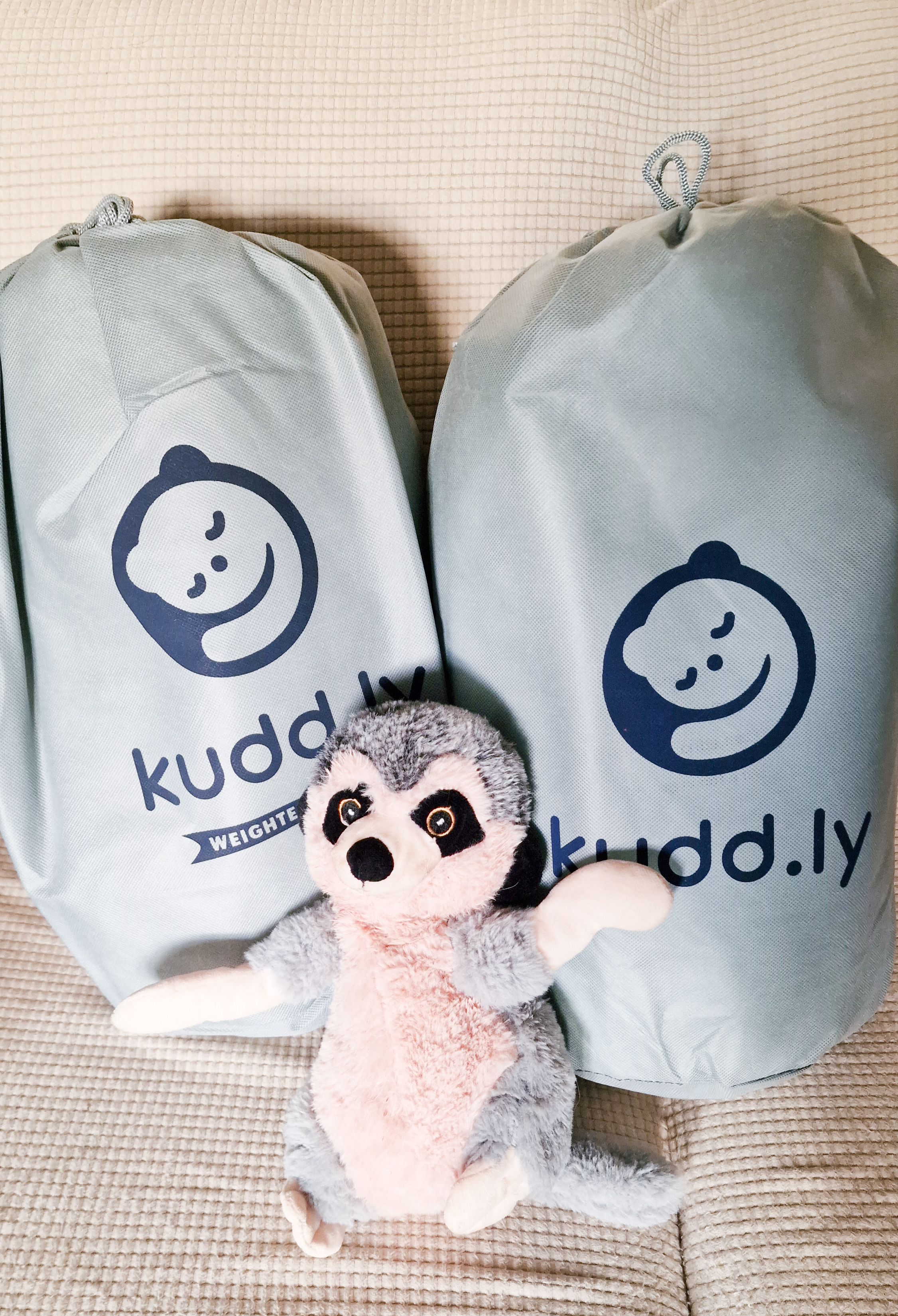 An image of two weighted blankets, still in their bags from delivery. The bags are grey and have a logo that looks like a sleepy bear cuddling, and the text reads &quot;Kuddly weighted blanket&quot;
