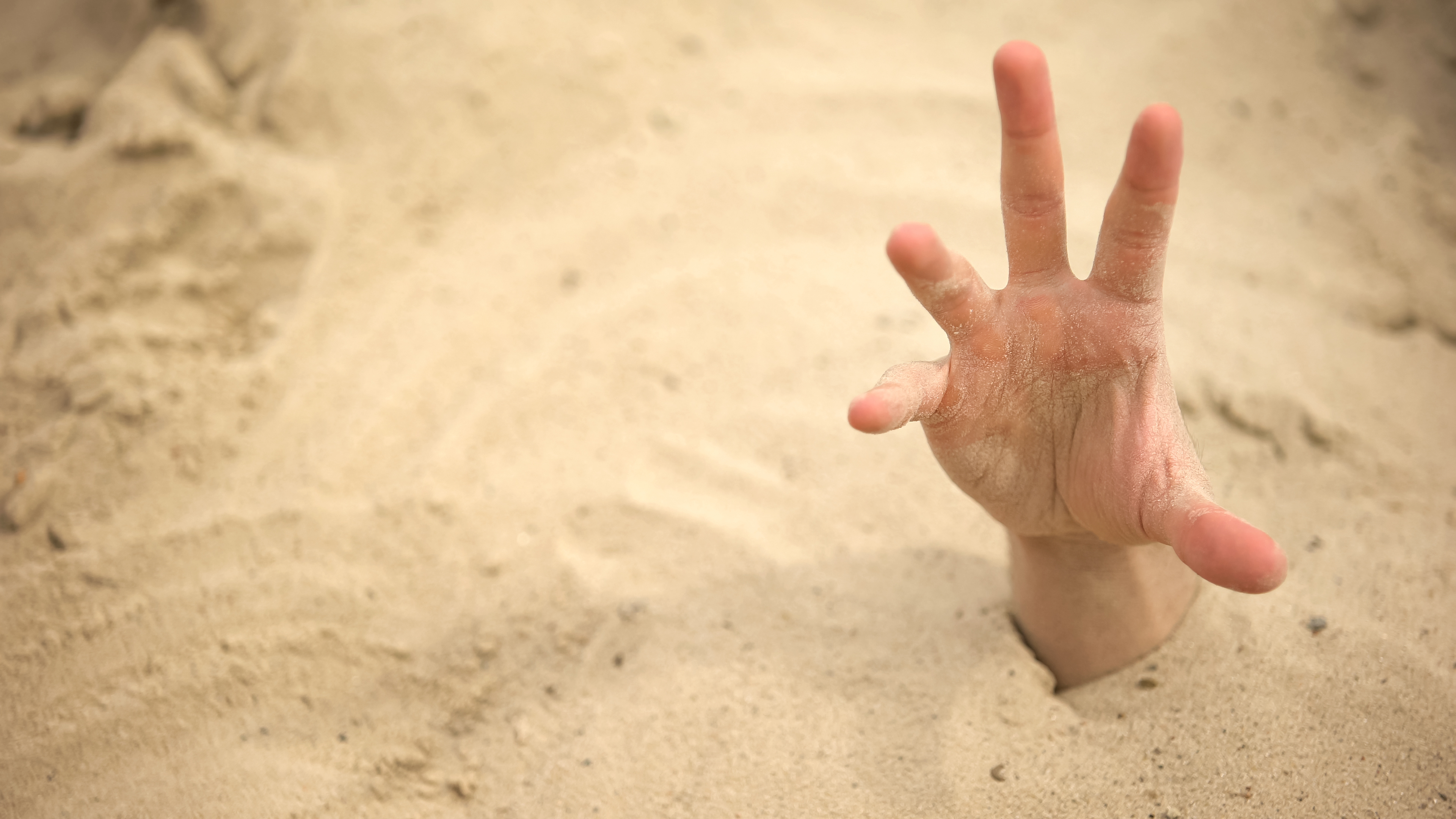 A hand sticking up out of the sand
