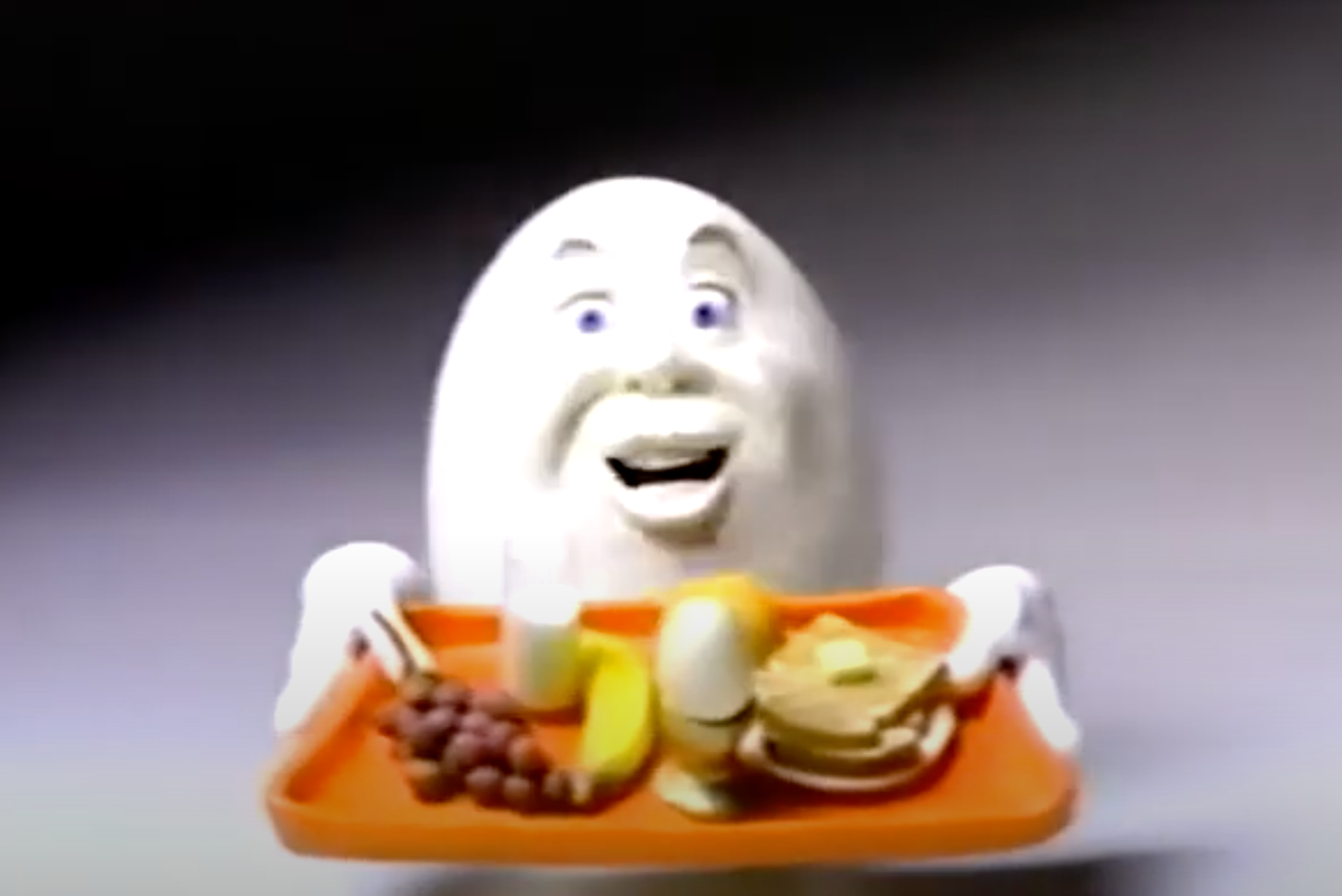 A cartoon egg holding a tray of food including an egg, toast, milk, and fruit