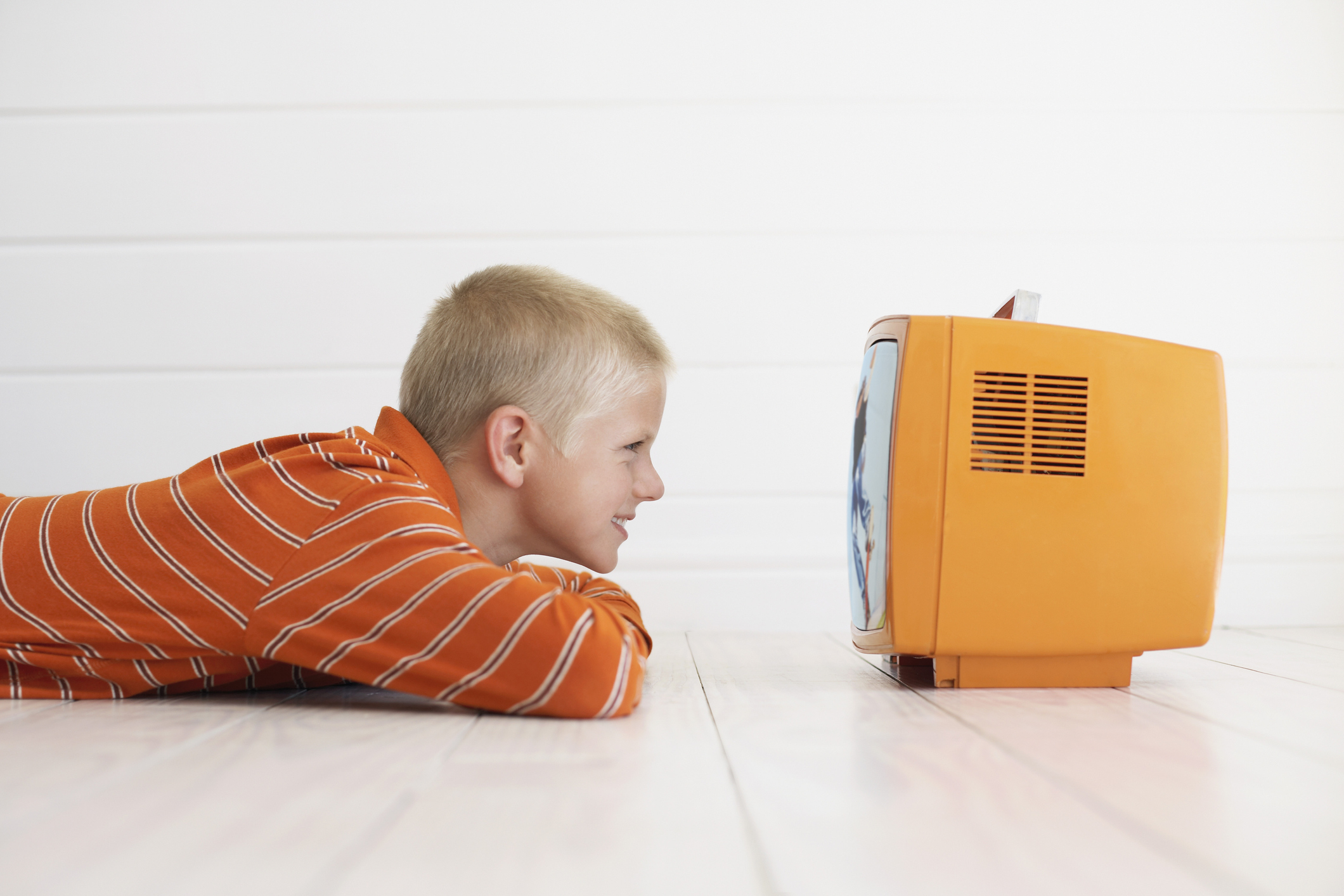 Child lying on their stomach on the floor and watching a small TV about 5 inches from their face